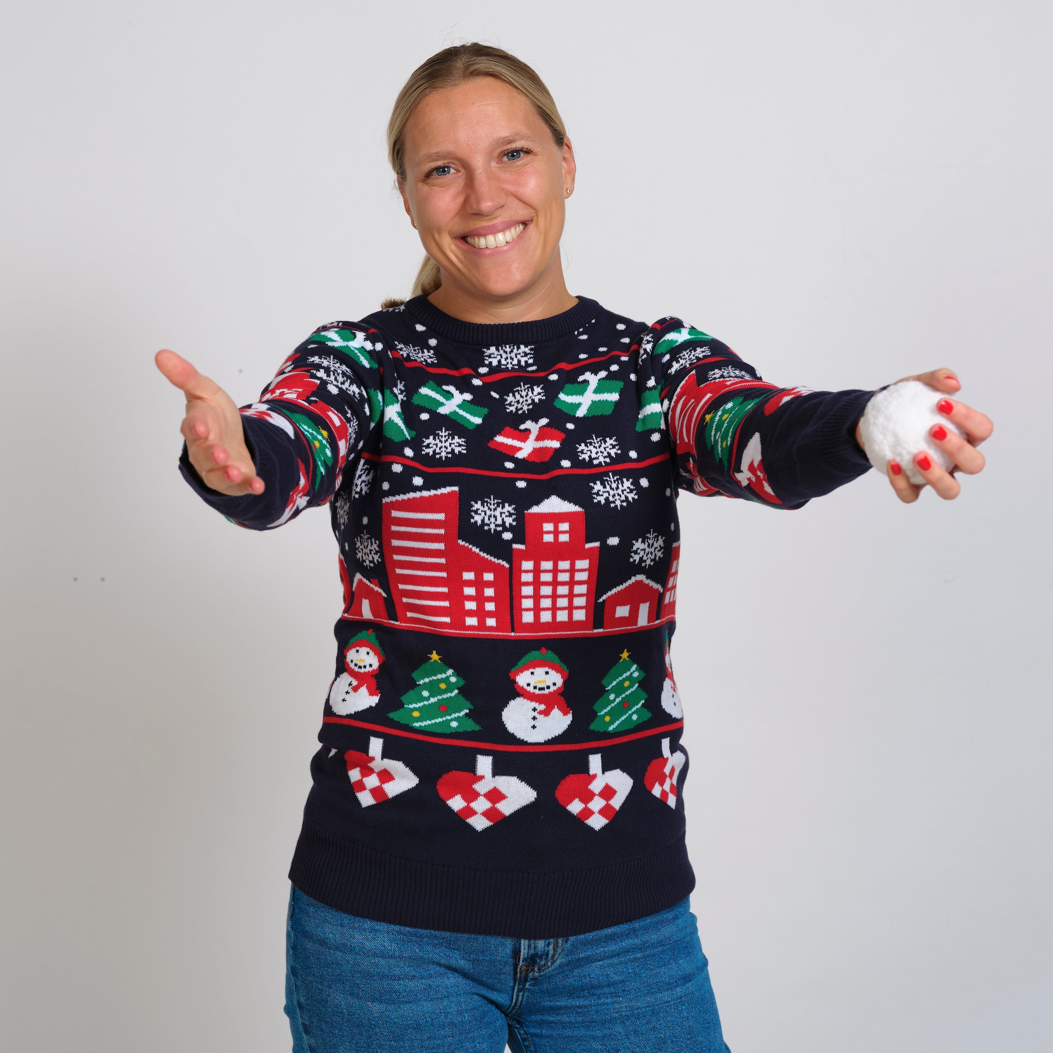 En dame med en snebold i hånden og en blå julesweater på.