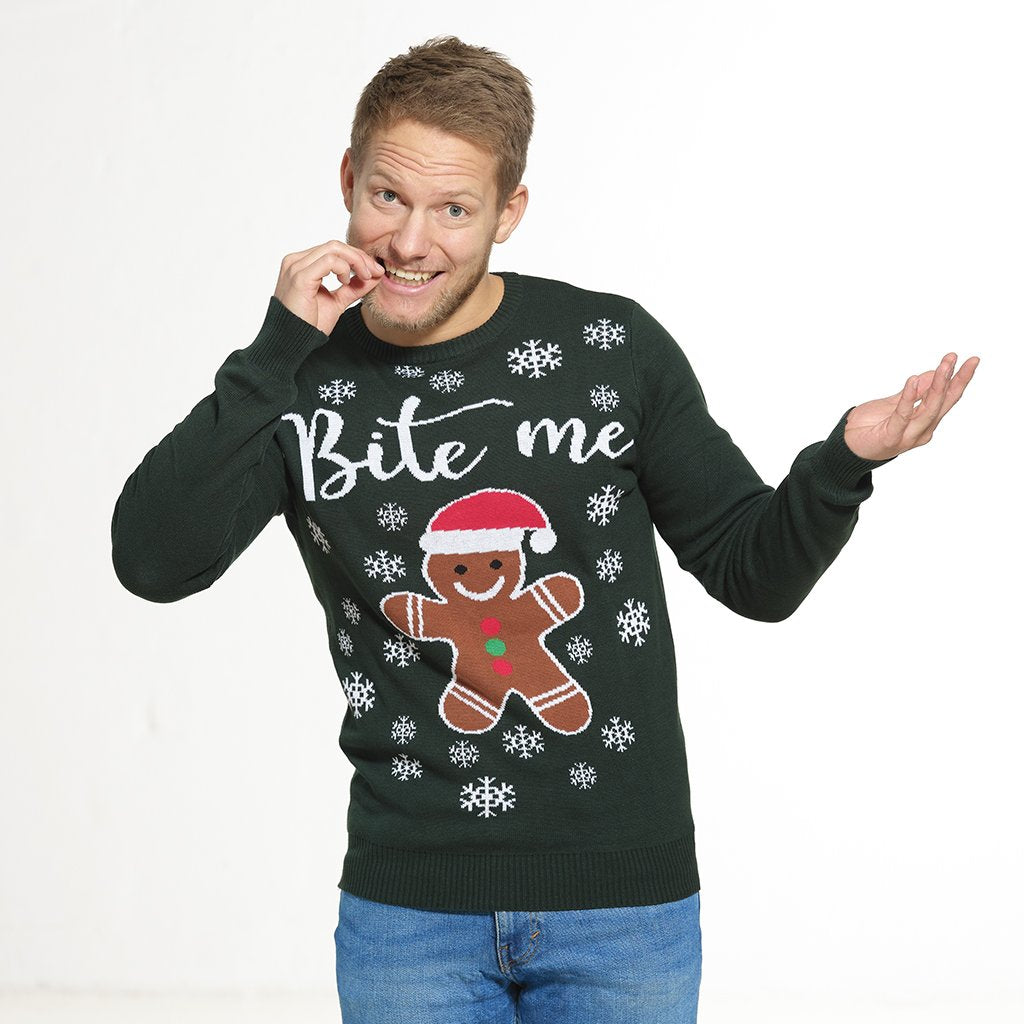 Un homme posant portant un pull vert de Noël avec un gâteau et la citation 