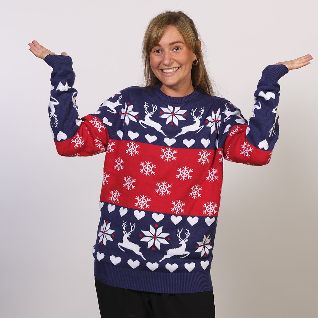 Une femme posant avec un pull de Noël bleu et rouge avec des rennes et un motif de Noël.