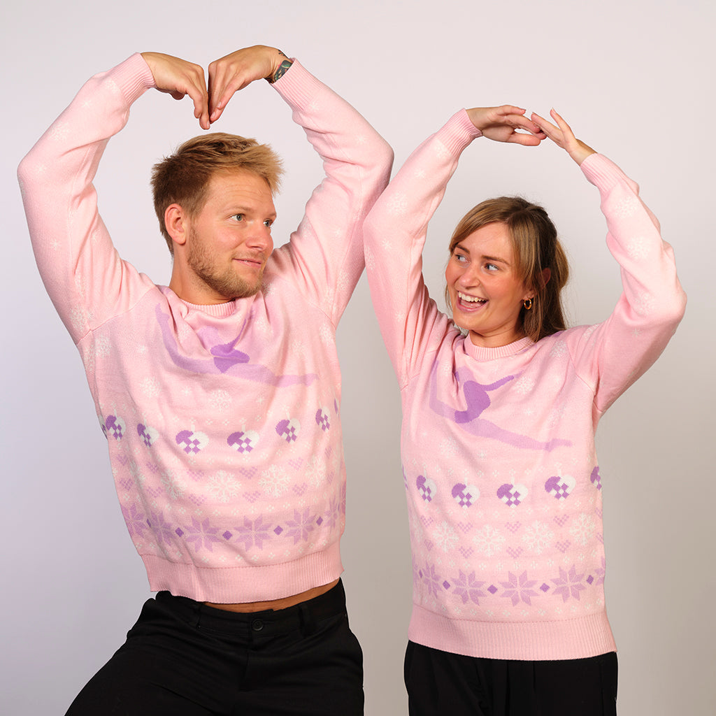 En mand og en kvinde poserer som balletdansere og er begge iført en lyserød julesweater.