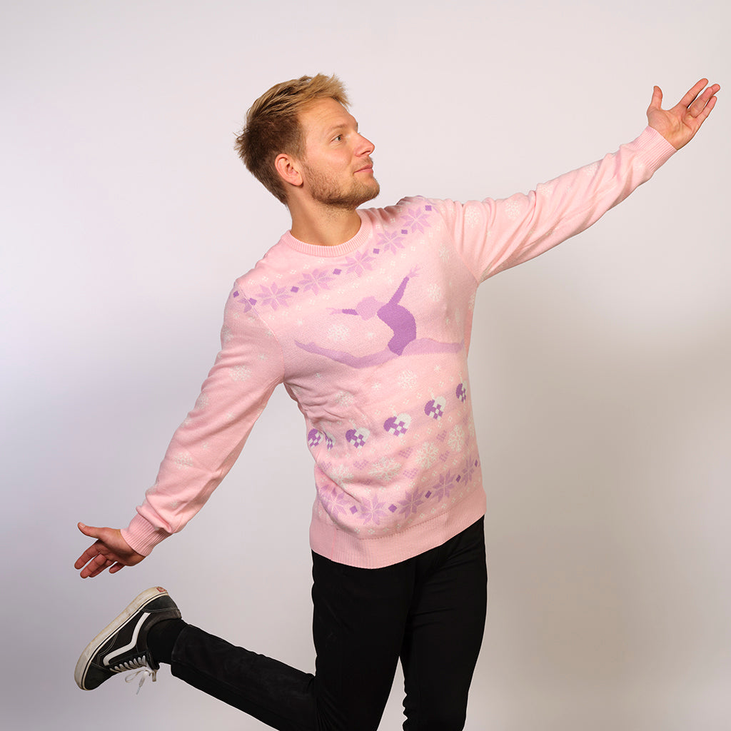 En mand poserer som en ballerina iført en lyserød julesweater med julehjerter på.