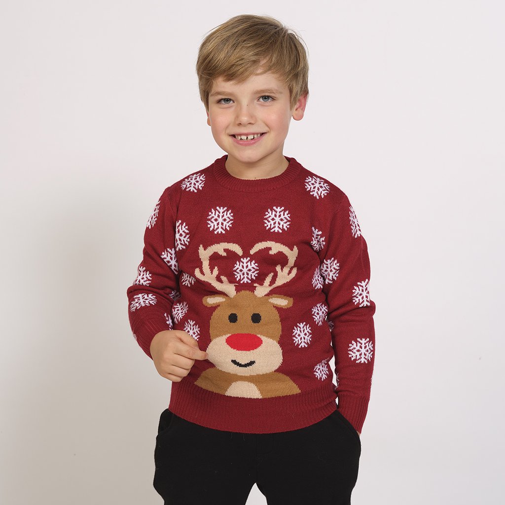 Un enfant portant un pull de Noël rouge foncé avec Rudolph et des flocons de neige.