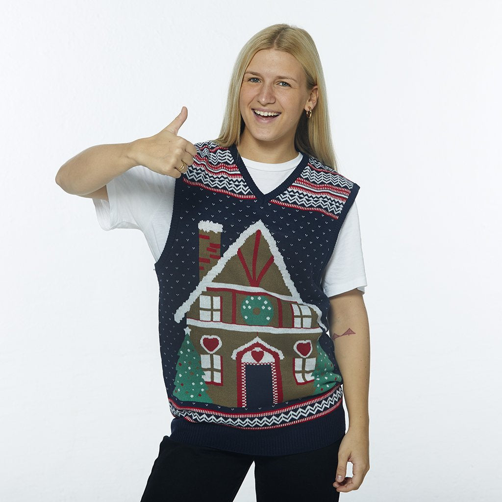 Une femme posant avec un gilet de Noël orné d'une maison en forme de gâteau.