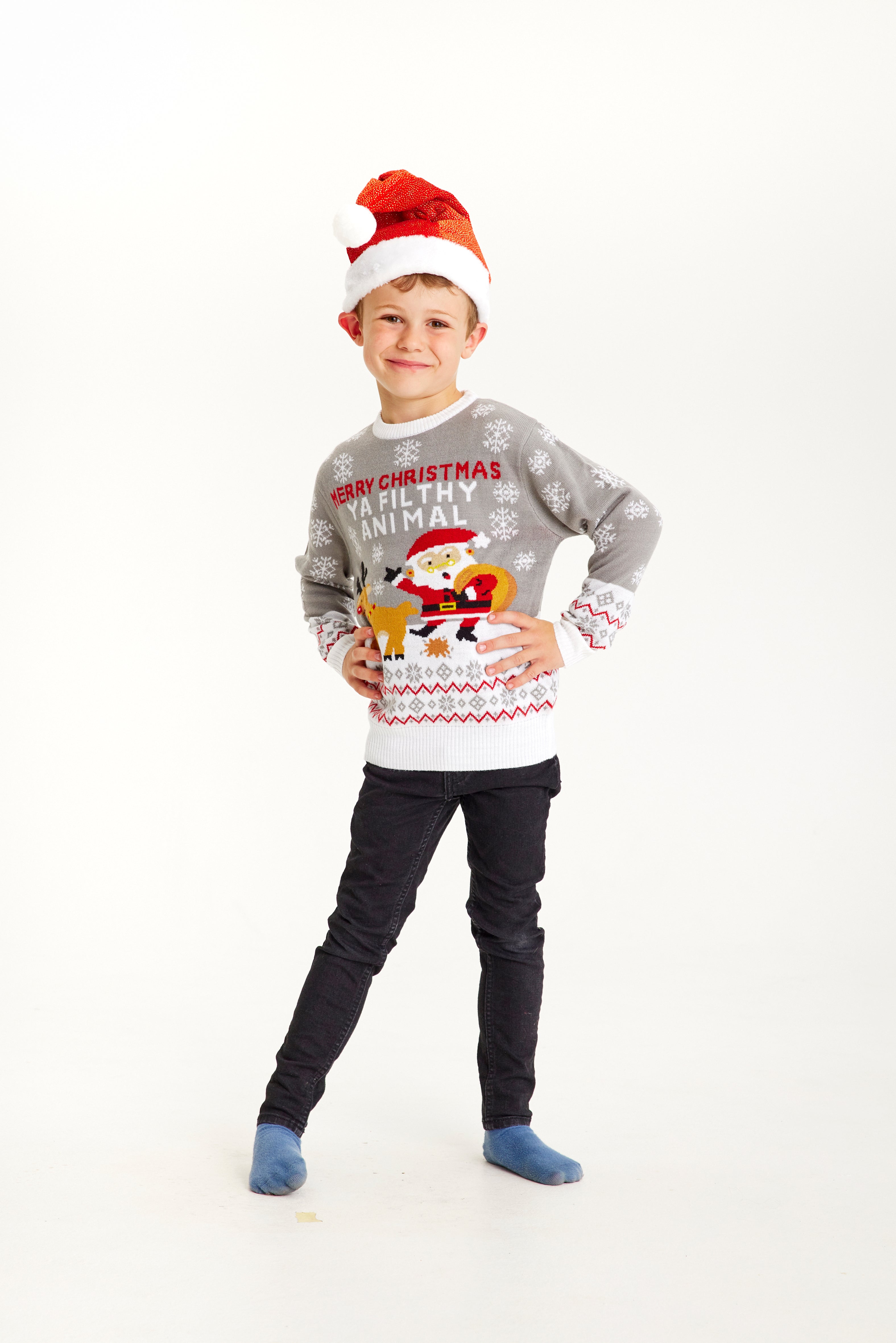 Un enfant, les mains le long du corps, vêtu d'un pull gris de Noël.