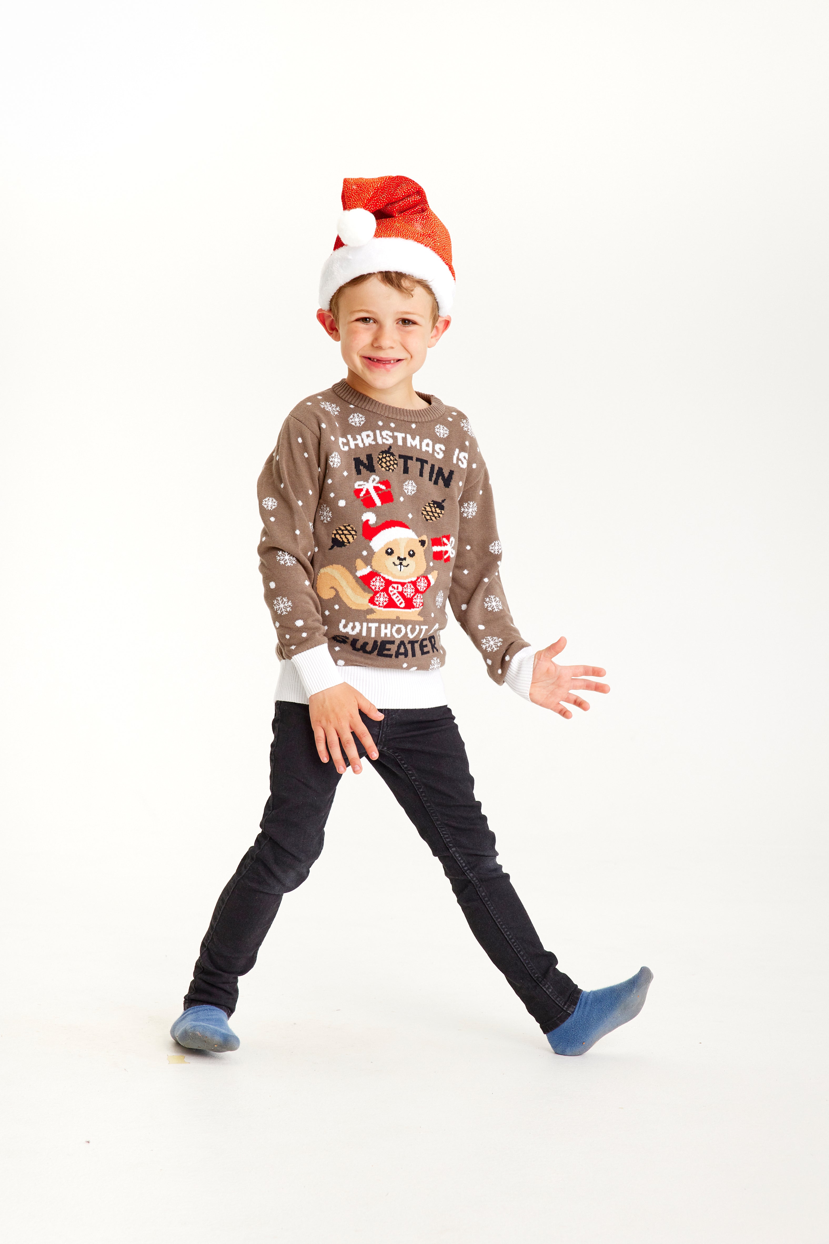 Un enfant qui pose, portant un pull de Noël marron avec la citation 