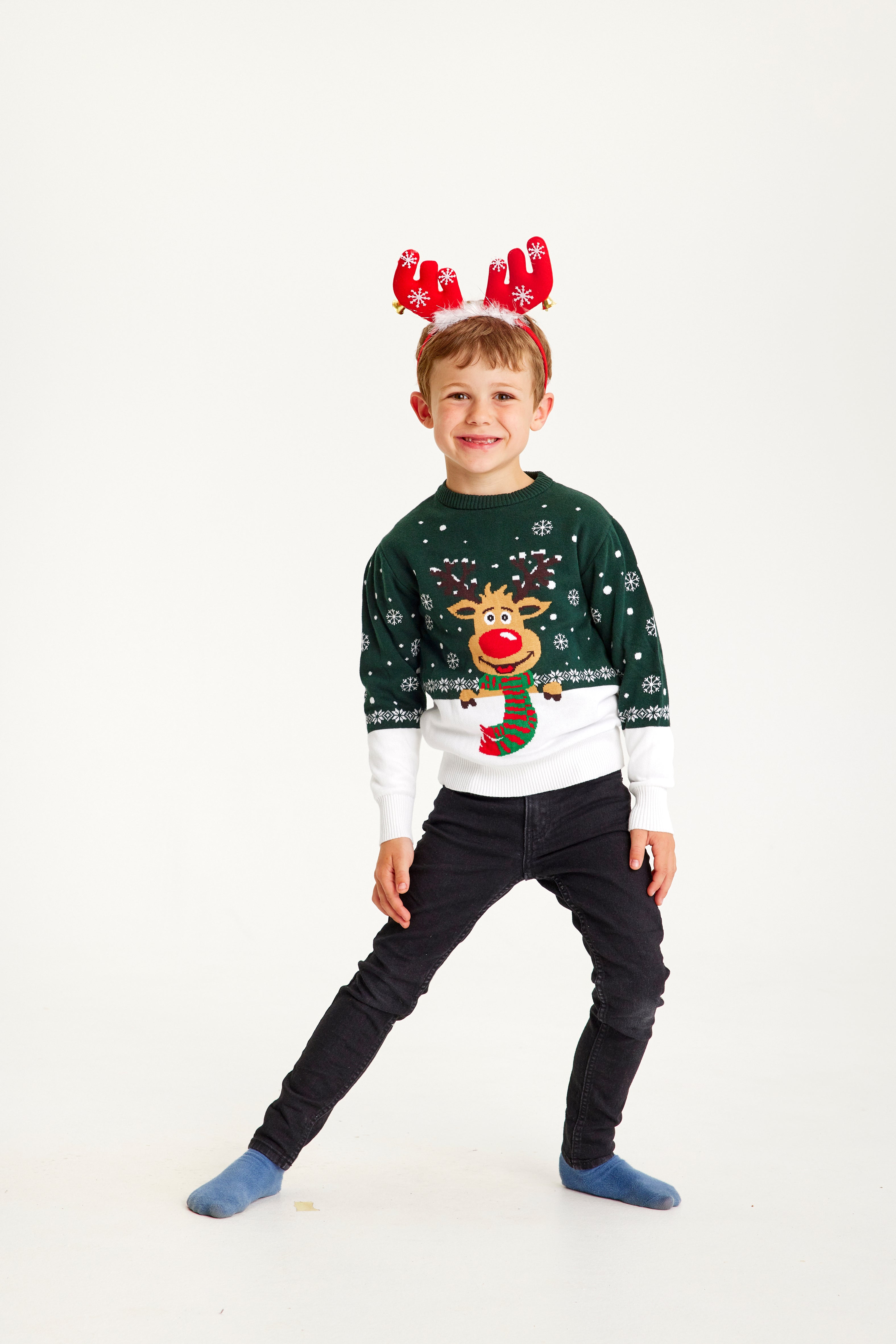 Un enfant posant avec un pull de Noël vert et blanc orné de Rudolph.