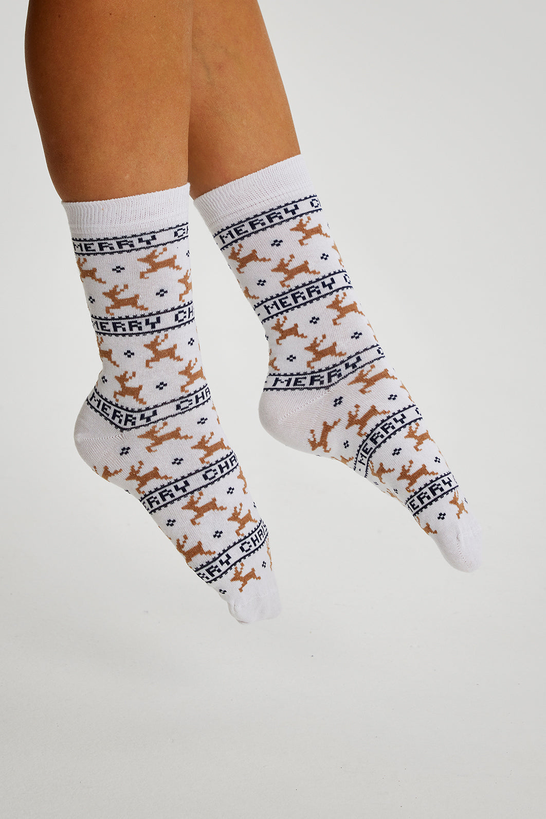 Een paar voeten met witte kerstsokken met rendieren erop.