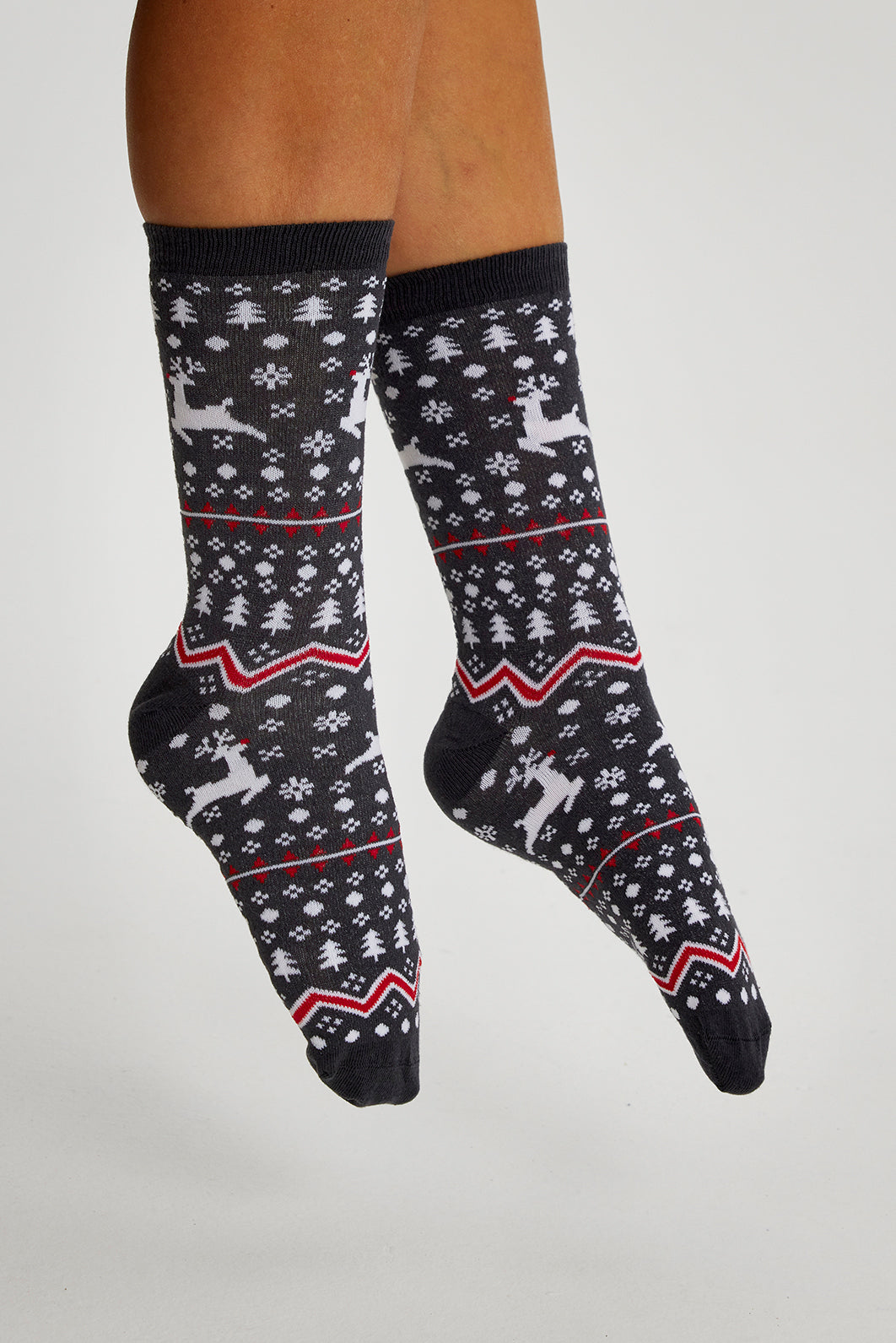 Een paar voeten met grijze kerstsokken met rendieren erop.