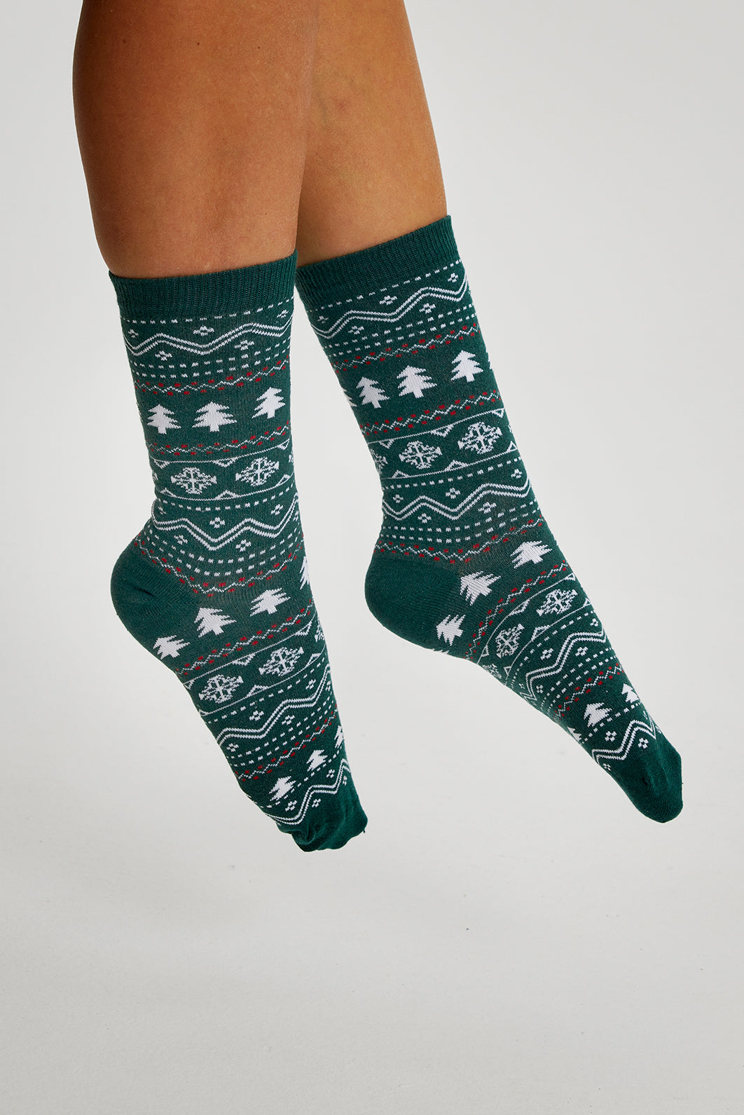 Une paire de pieds portant des chaussettes de Noël à motifs verts.