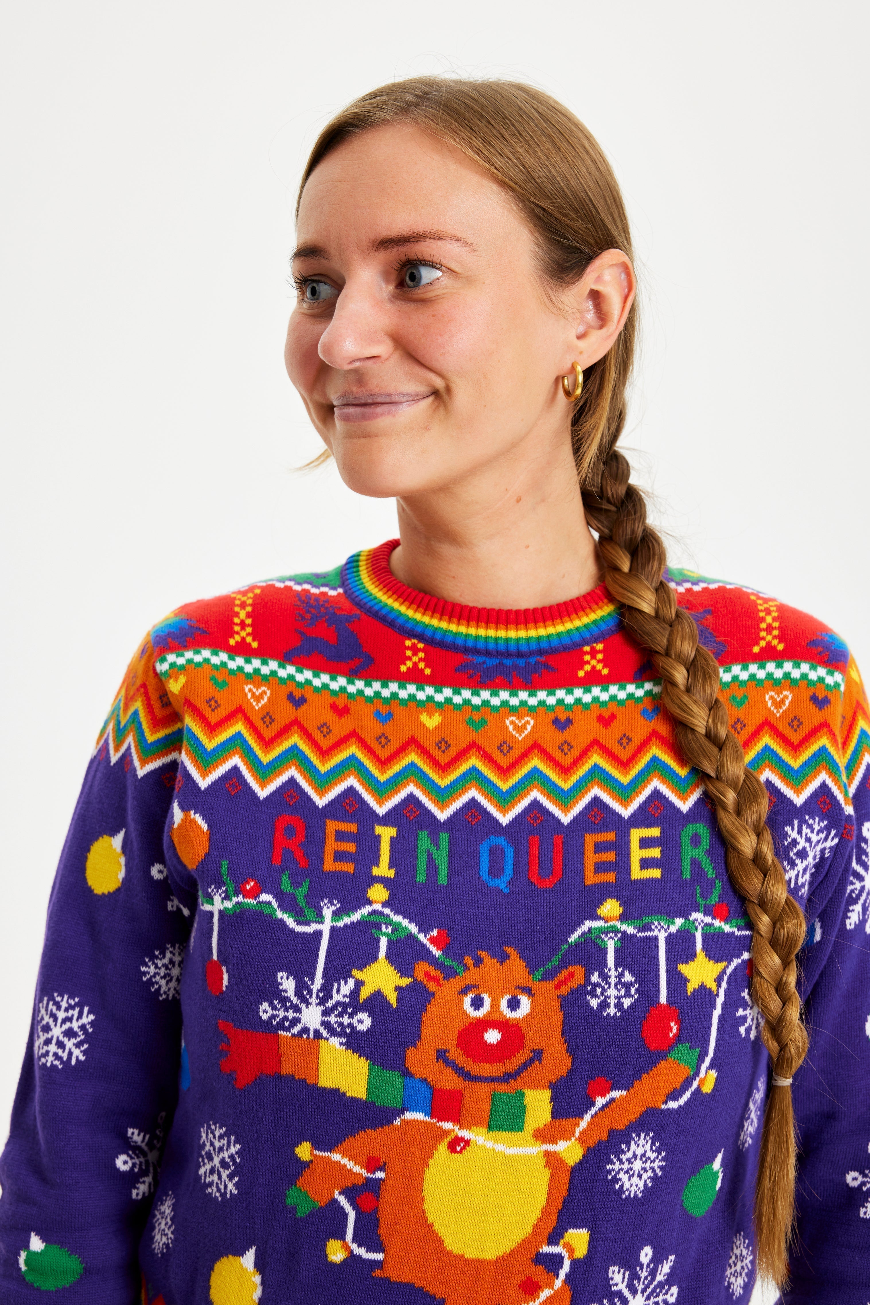 Une femme souriante portant un pull de Noël aux couleurs de l'arc-en-ciel avec la citation 