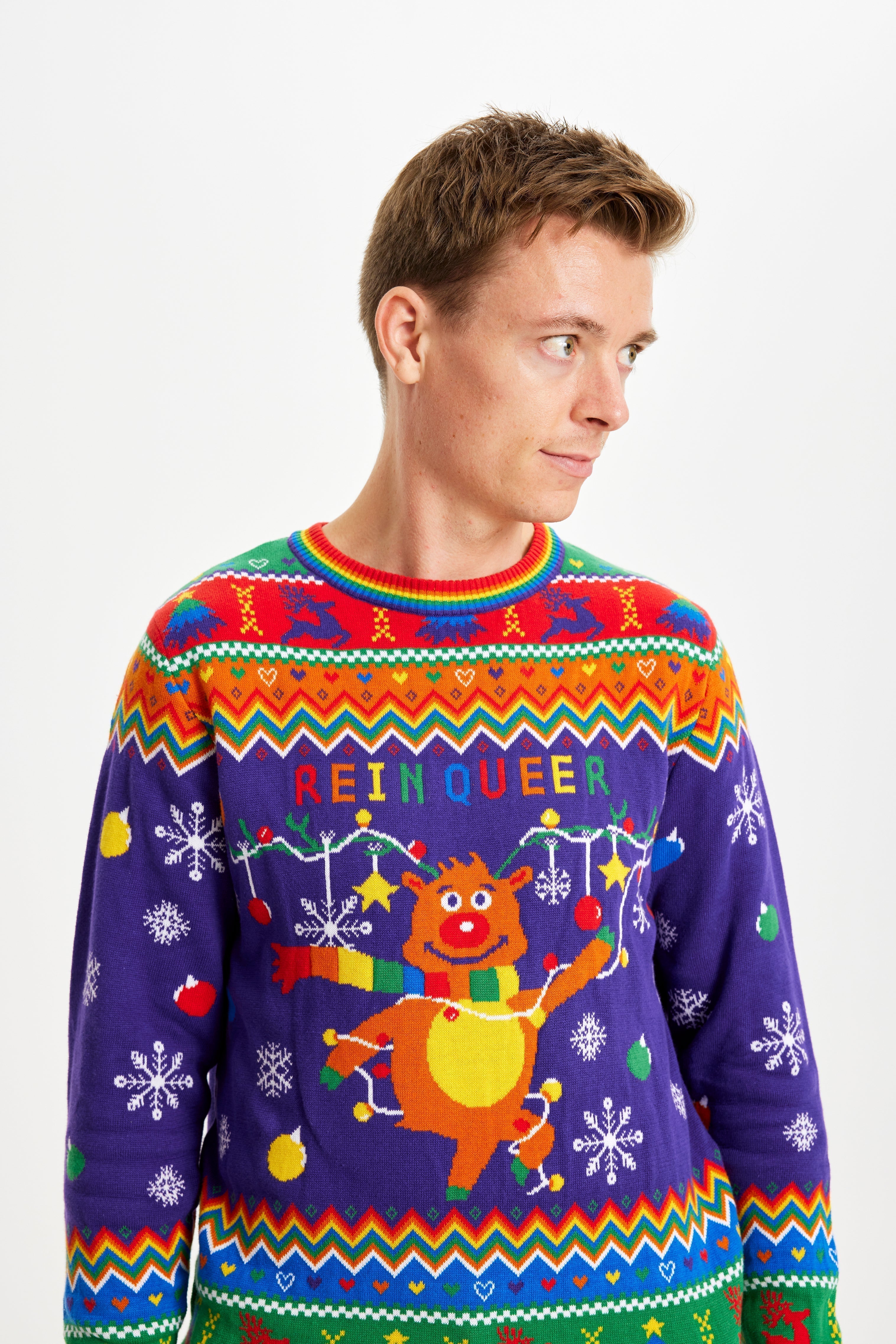 Un homme regardant sur le côté portant un pull de Noël aux couleurs de l'arc-en-ciel avec la citation 