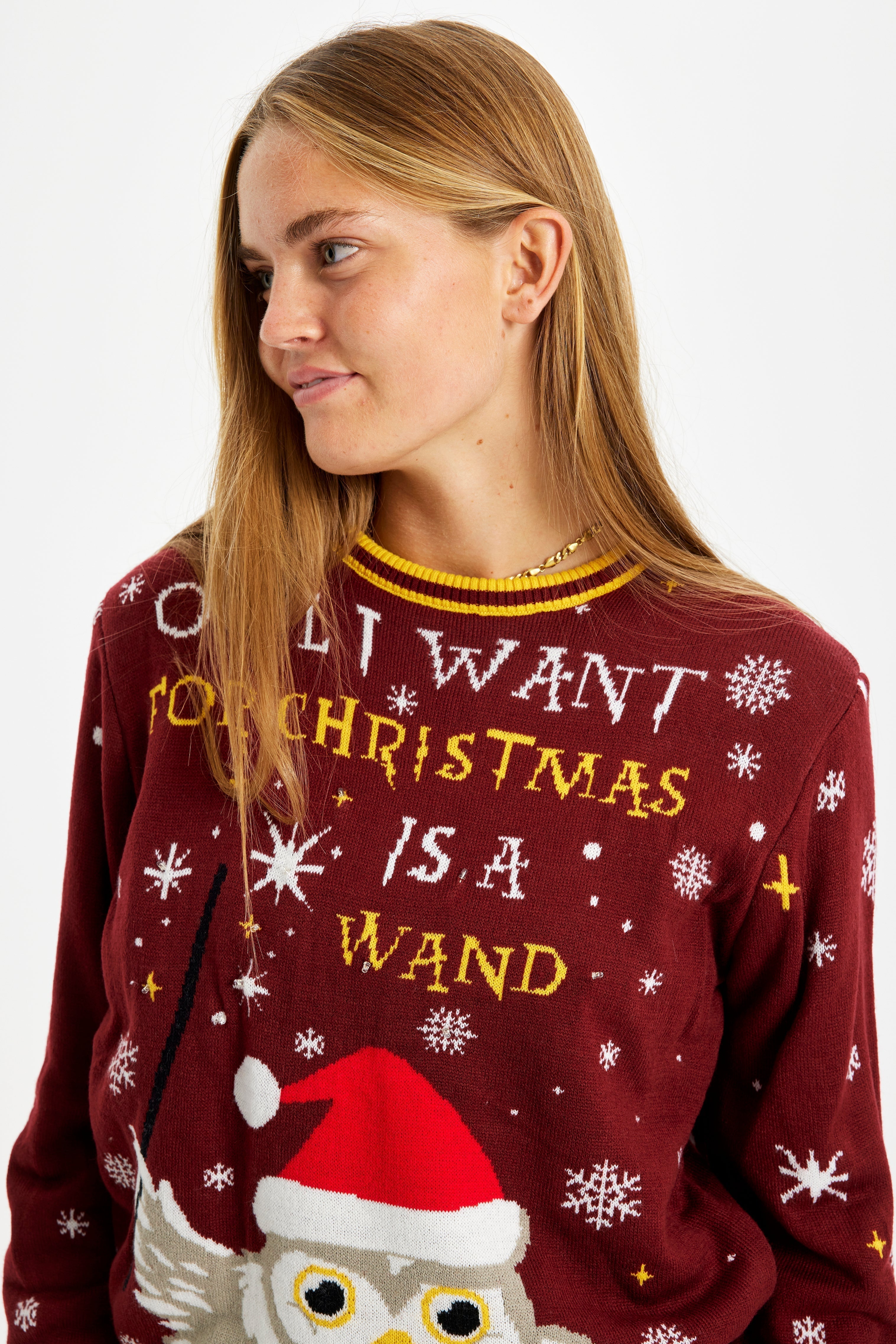 Une femme regarde sur le côté, vêtue d'un pull de Noël rouge avec la citation 