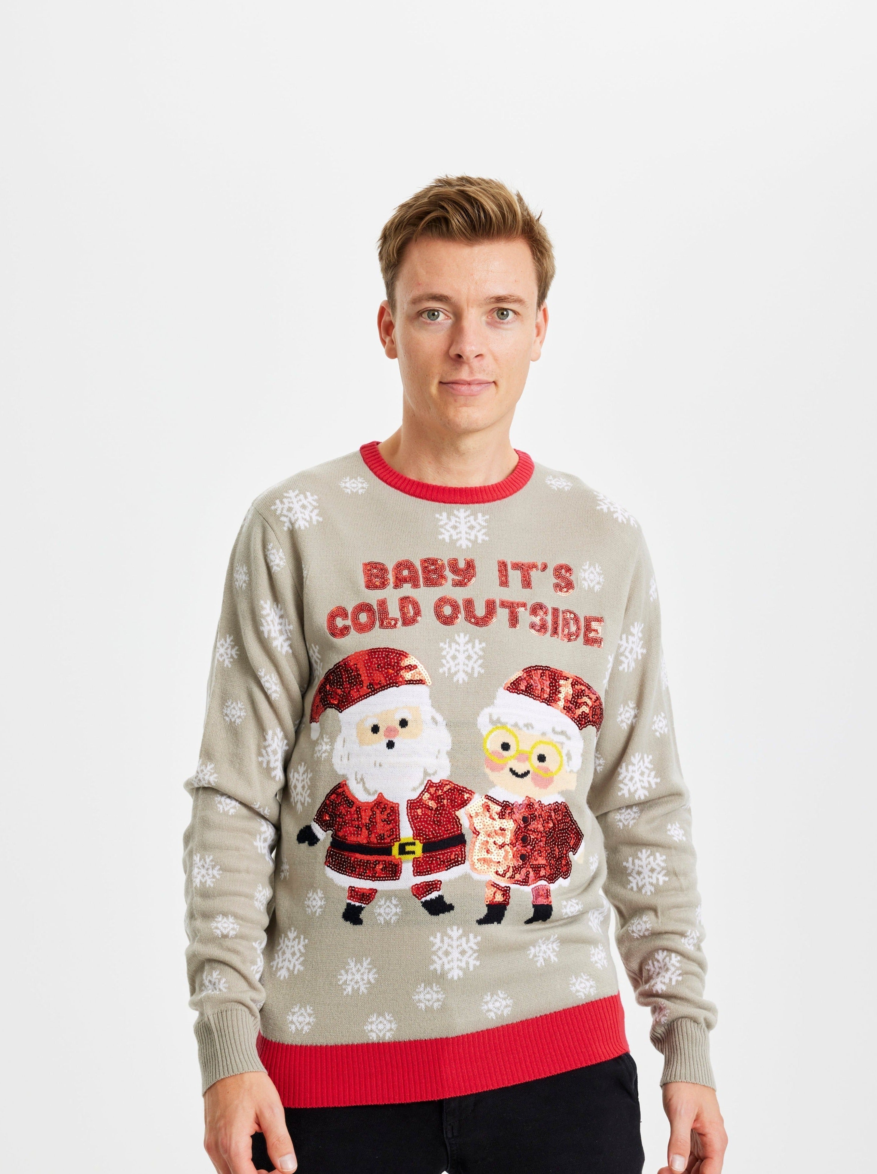 Un homme qui pose, portant un pull de Noël gris avec la citation 