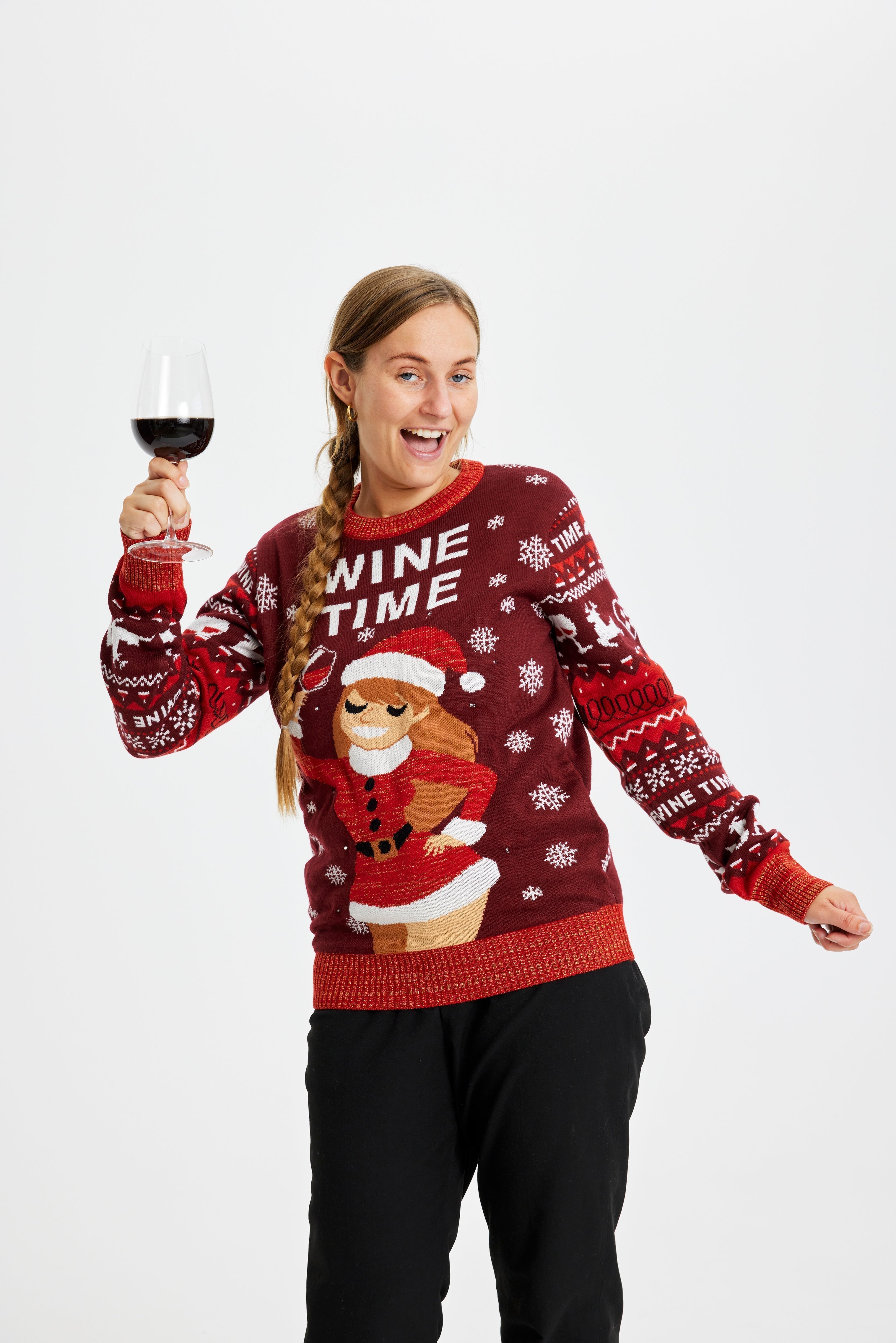 Une femme posant avec un verre de vin et portant un pull rouge de Noël avec la citation 