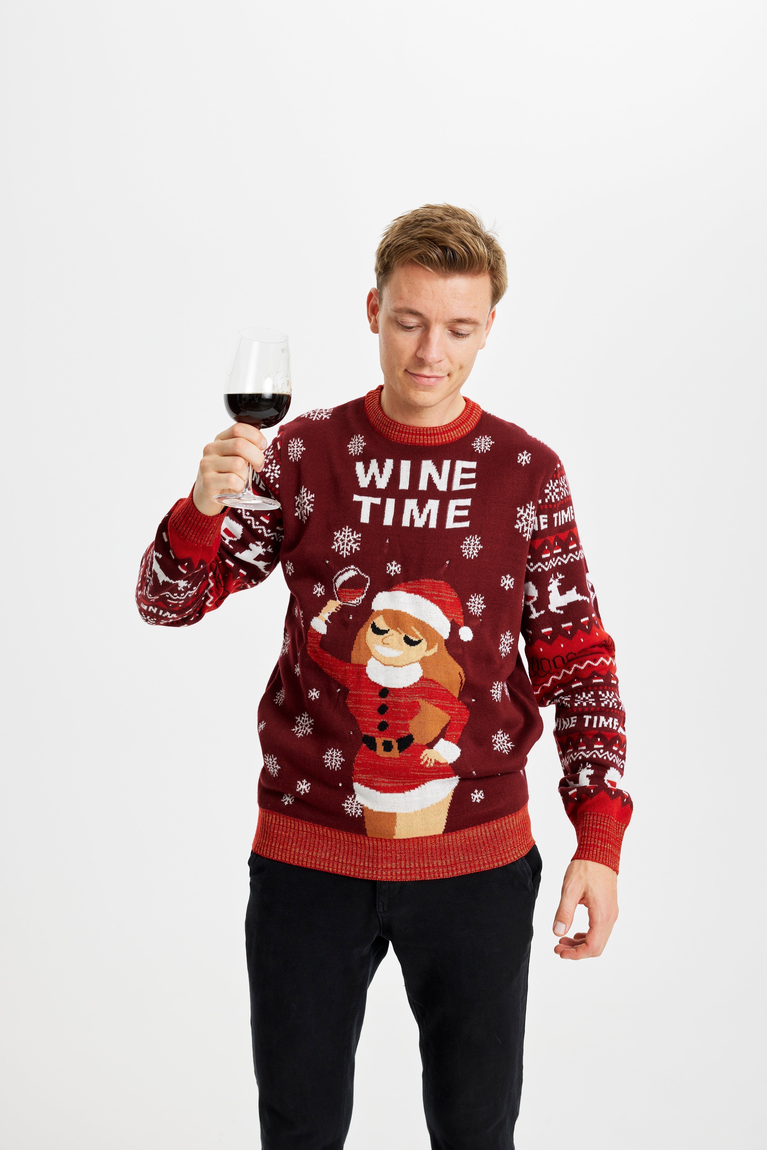 Un homme posant avec un verre de vin et portant un pull de Noël rouge avec la citation 