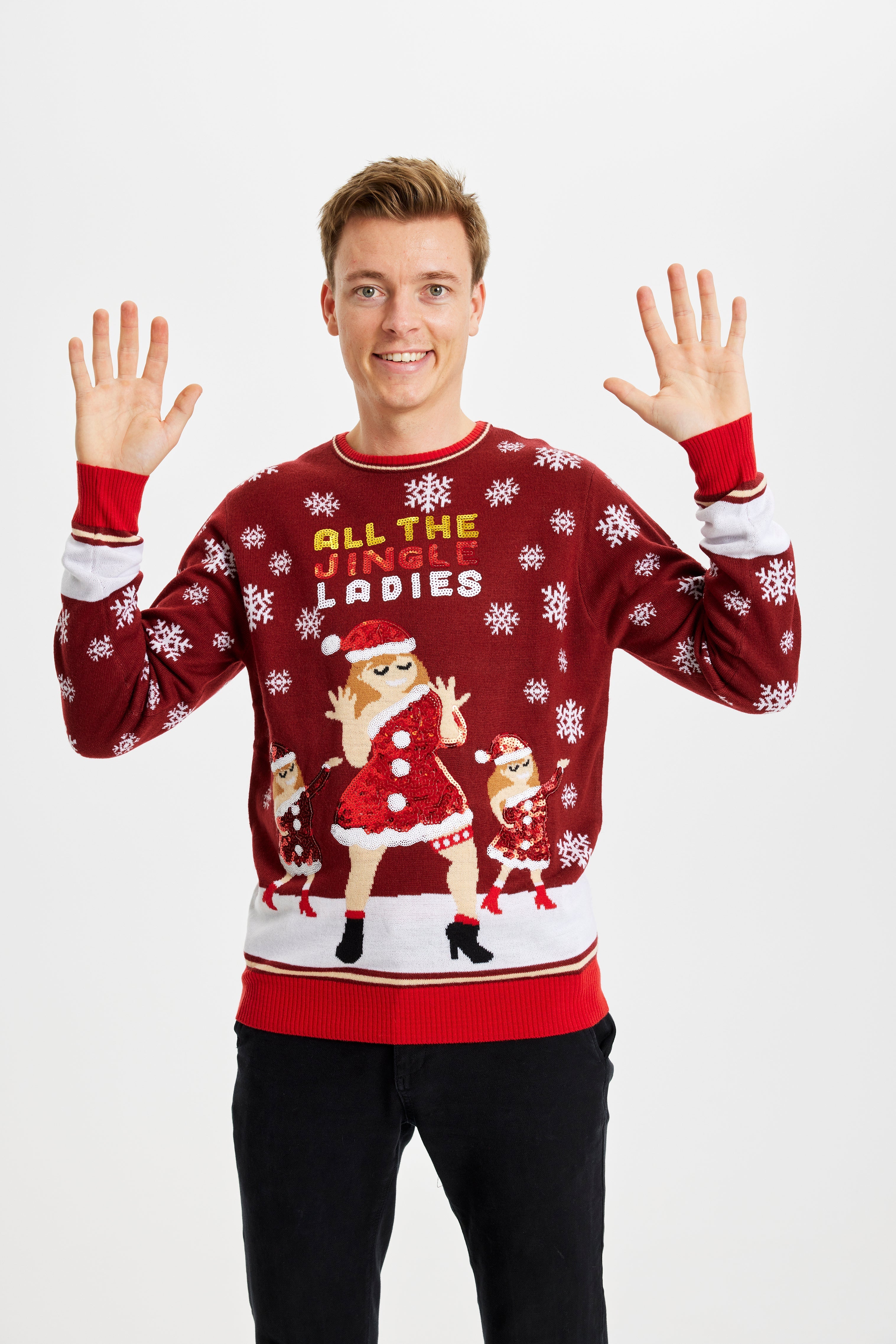 En mand med hænderne i vejret, der har en rød julesweater med snefnug og dansende kvinder på.