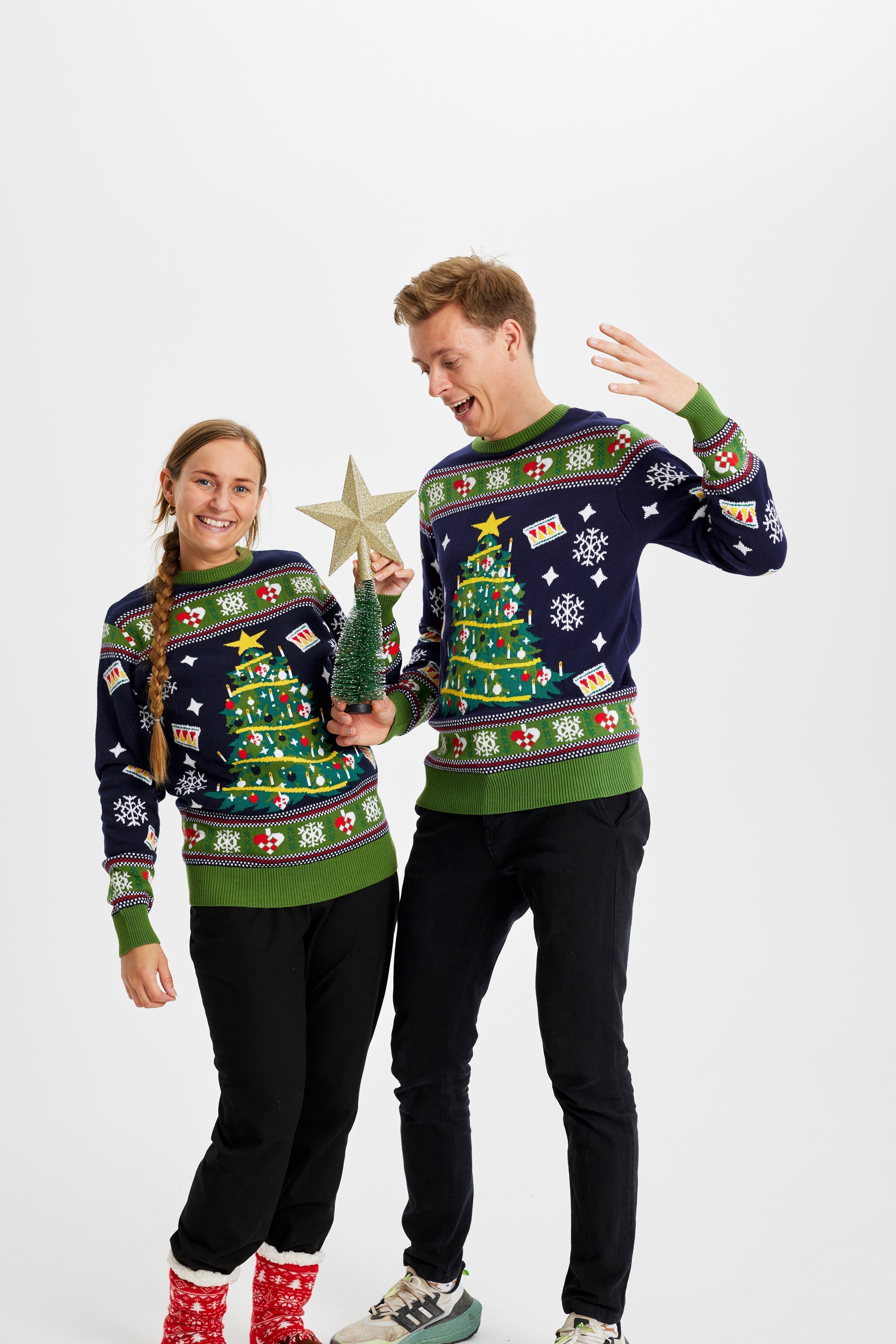 Un couple portant un pull bleu et vert avec un sapin de Noël.