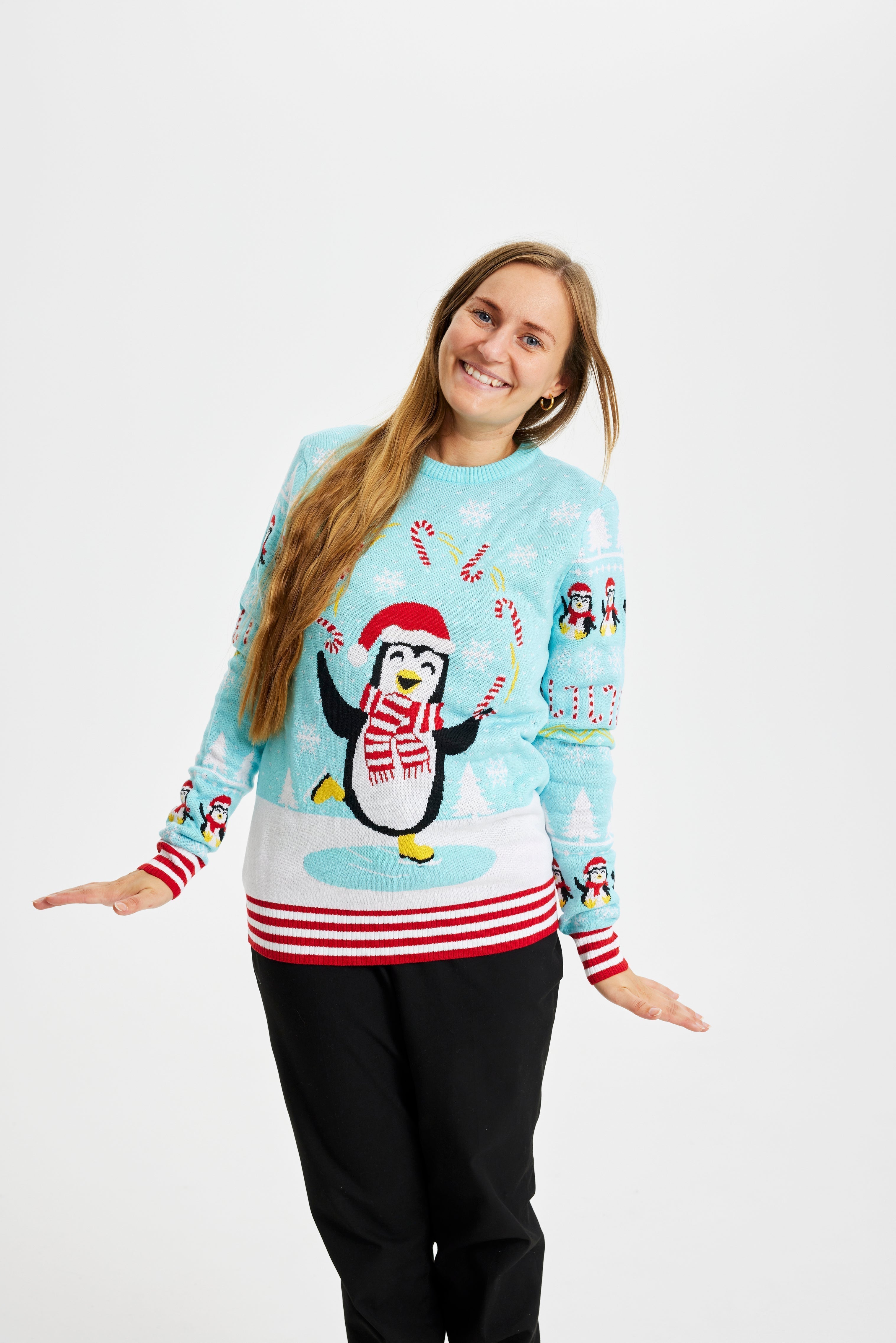 Une femme posant avec un pull de Noël bleu clair avec des pingouins et des lumières.