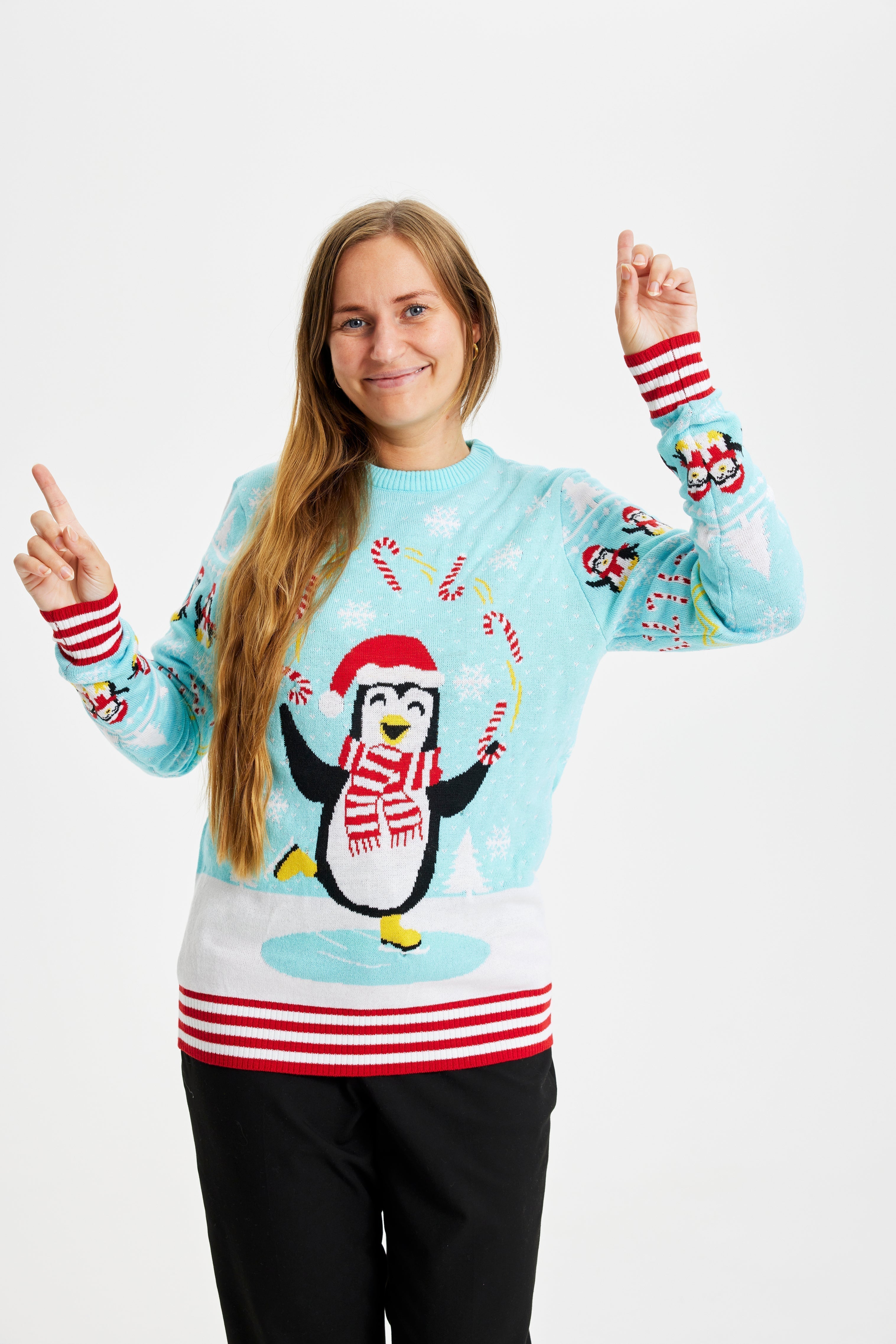 Une femme souriante portant un pull de Noël bleu clair avec des pingouins et des lumières.