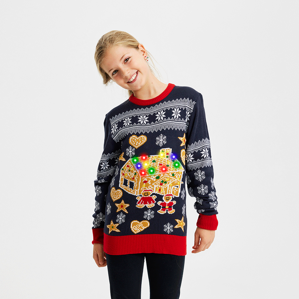 Et barn iført en mørkeblå julesweater med et kagehus med lys på.