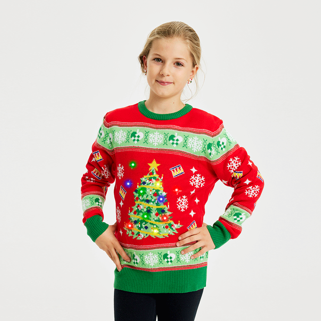 Un enfant portant un pull de Noël rouge et vert avec un arbre de Noël et des lumières.