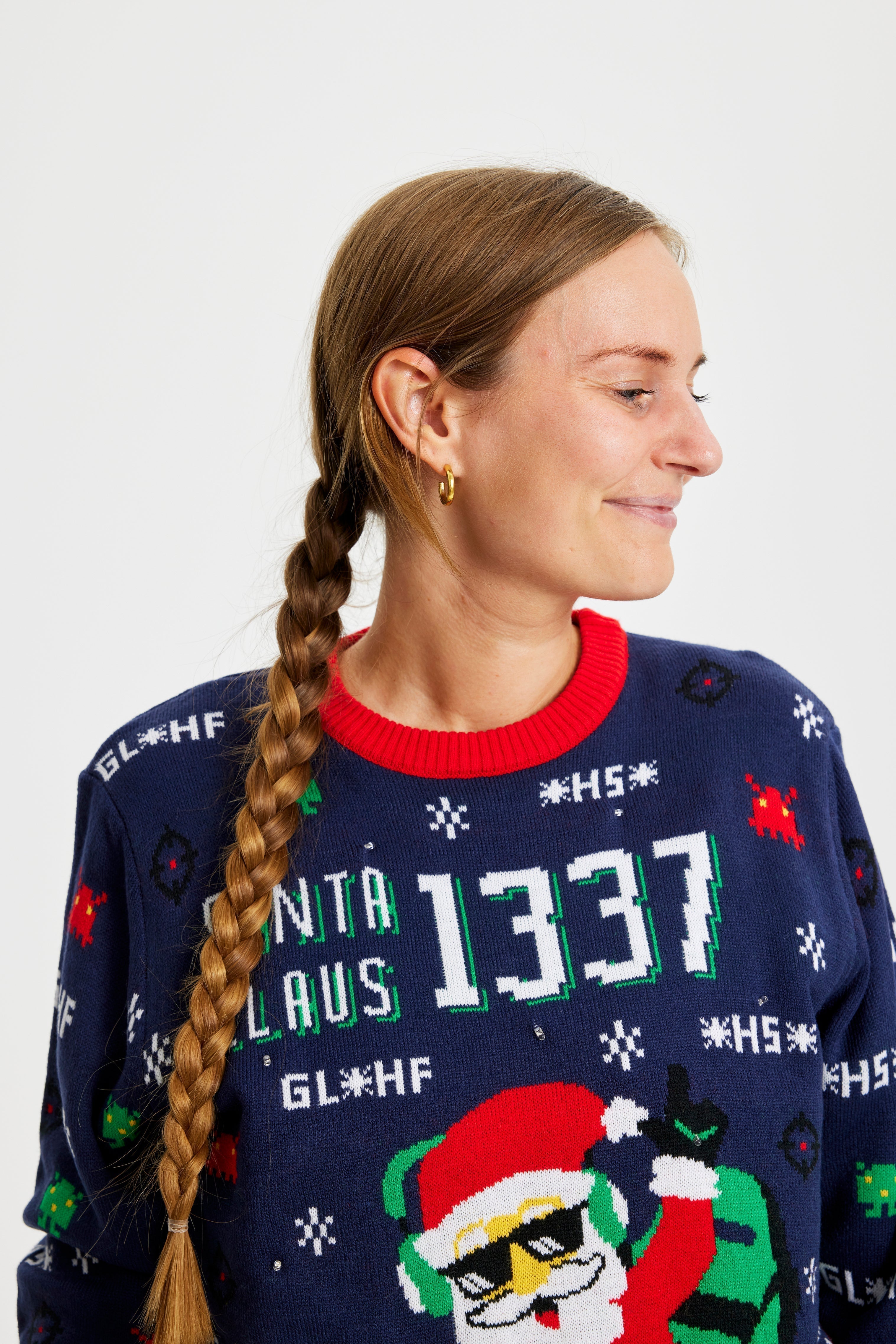 Une femme regardant sur le côté portant un pull de Noël bleu et rouge avec un Père Noël et des lumières.