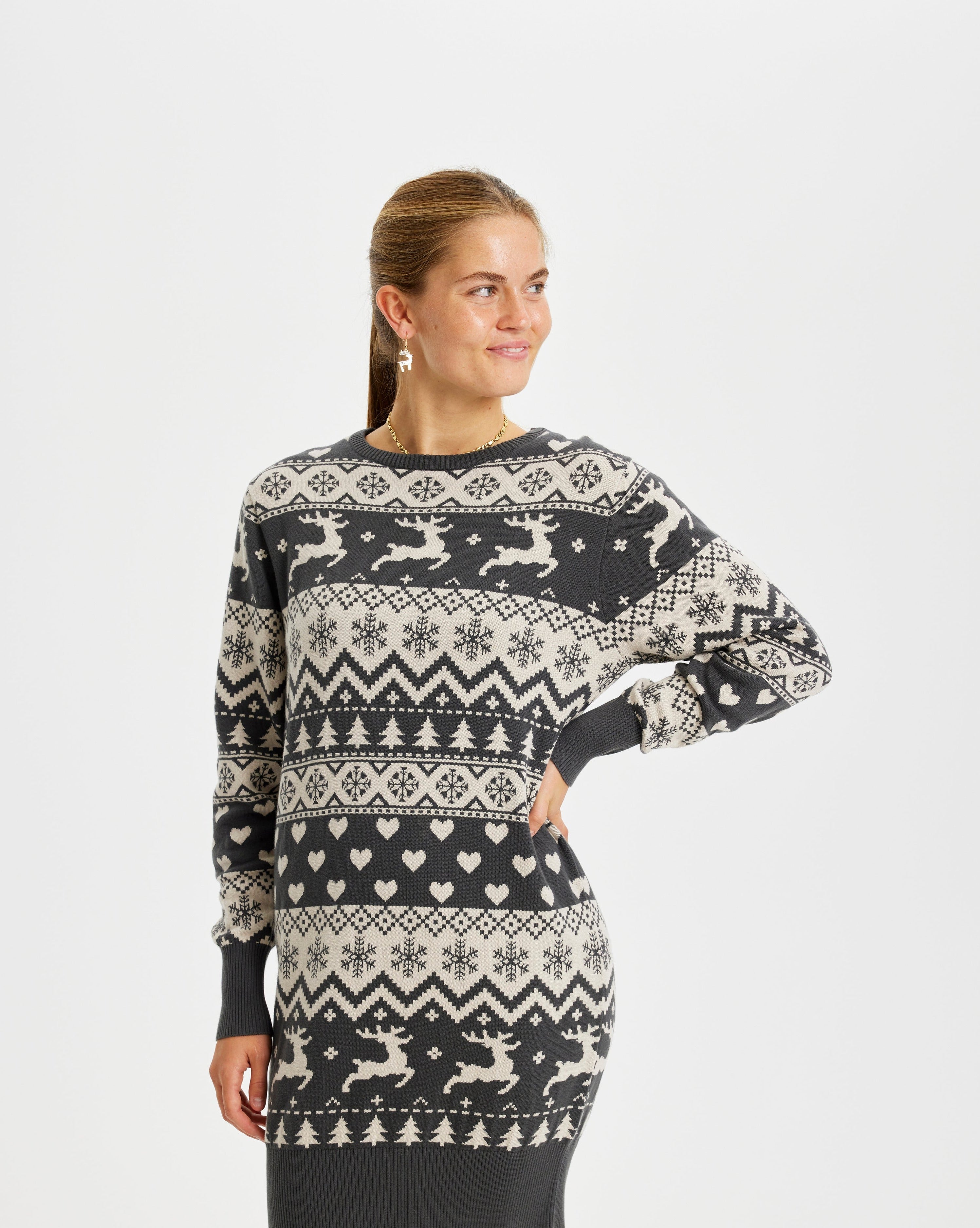 Une femme regarde de côté, vêtue d'une robe de Noël à rayures grises avec des rennes et un motif de Noël.