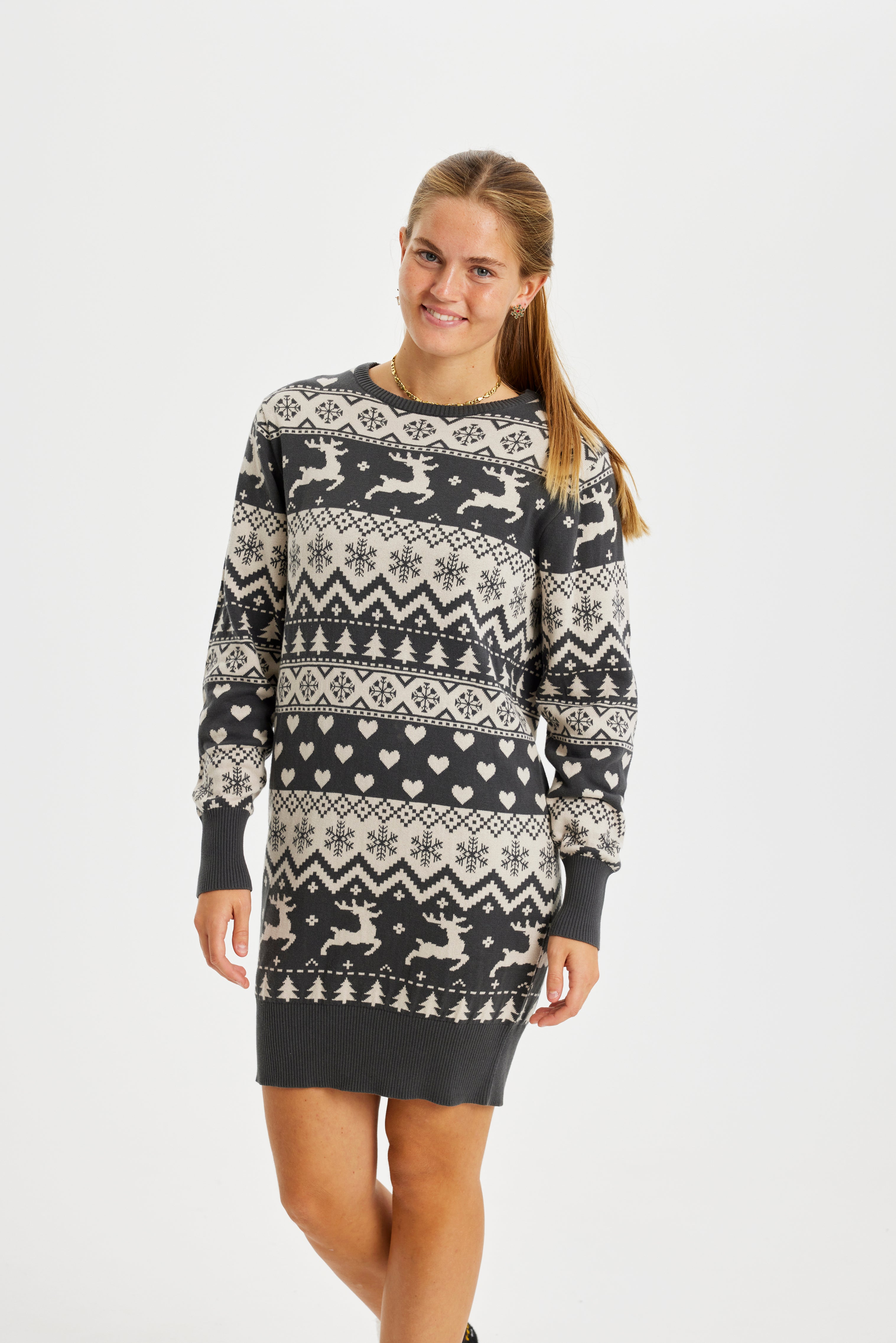 Une femme souriante portant une robe de Noël à rayures grises avec des rennes et un motif de Noël.