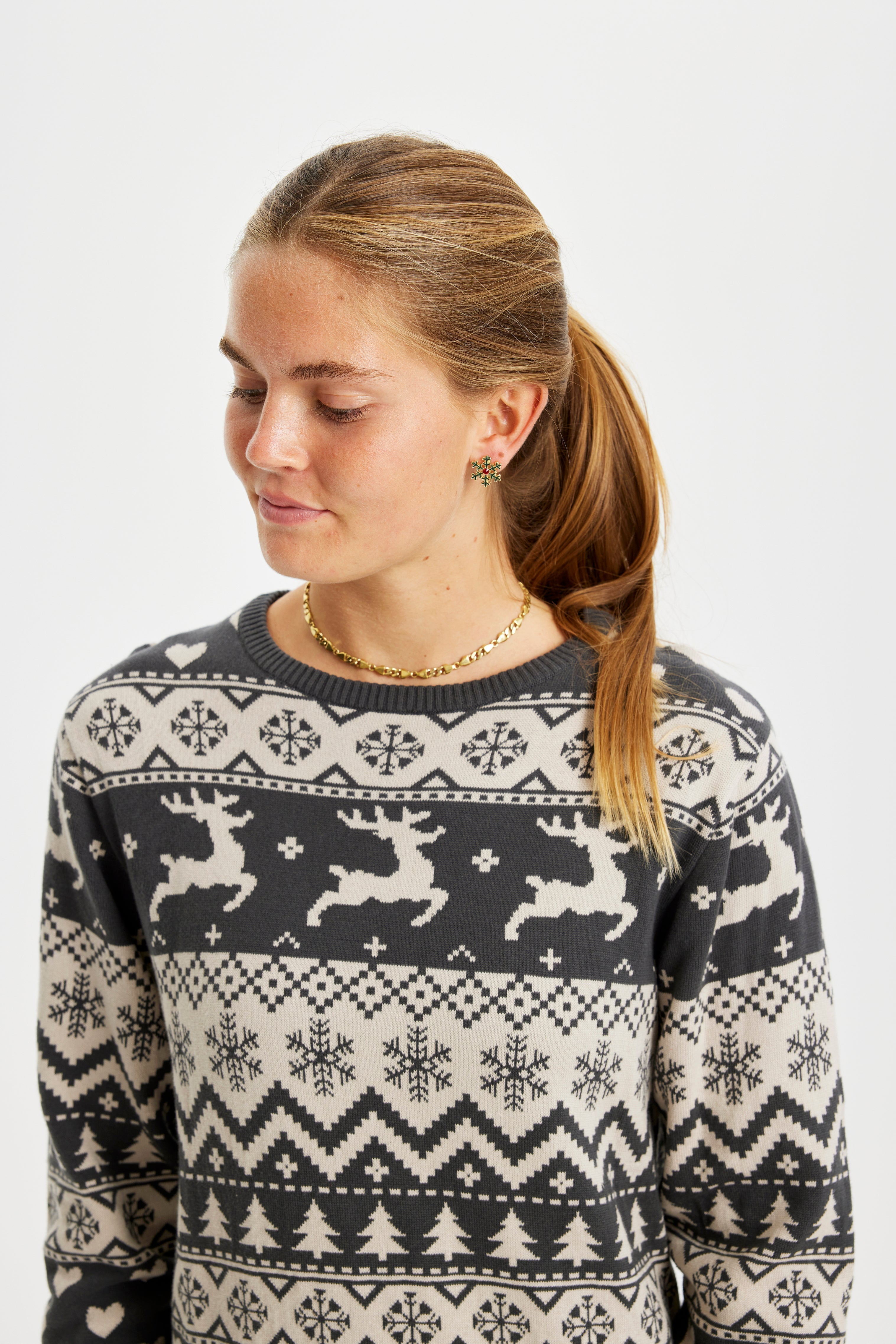 Une femme regardant vers le bas portant une robe de Noël à rayures grises avec des rennes et un motif de Noël.