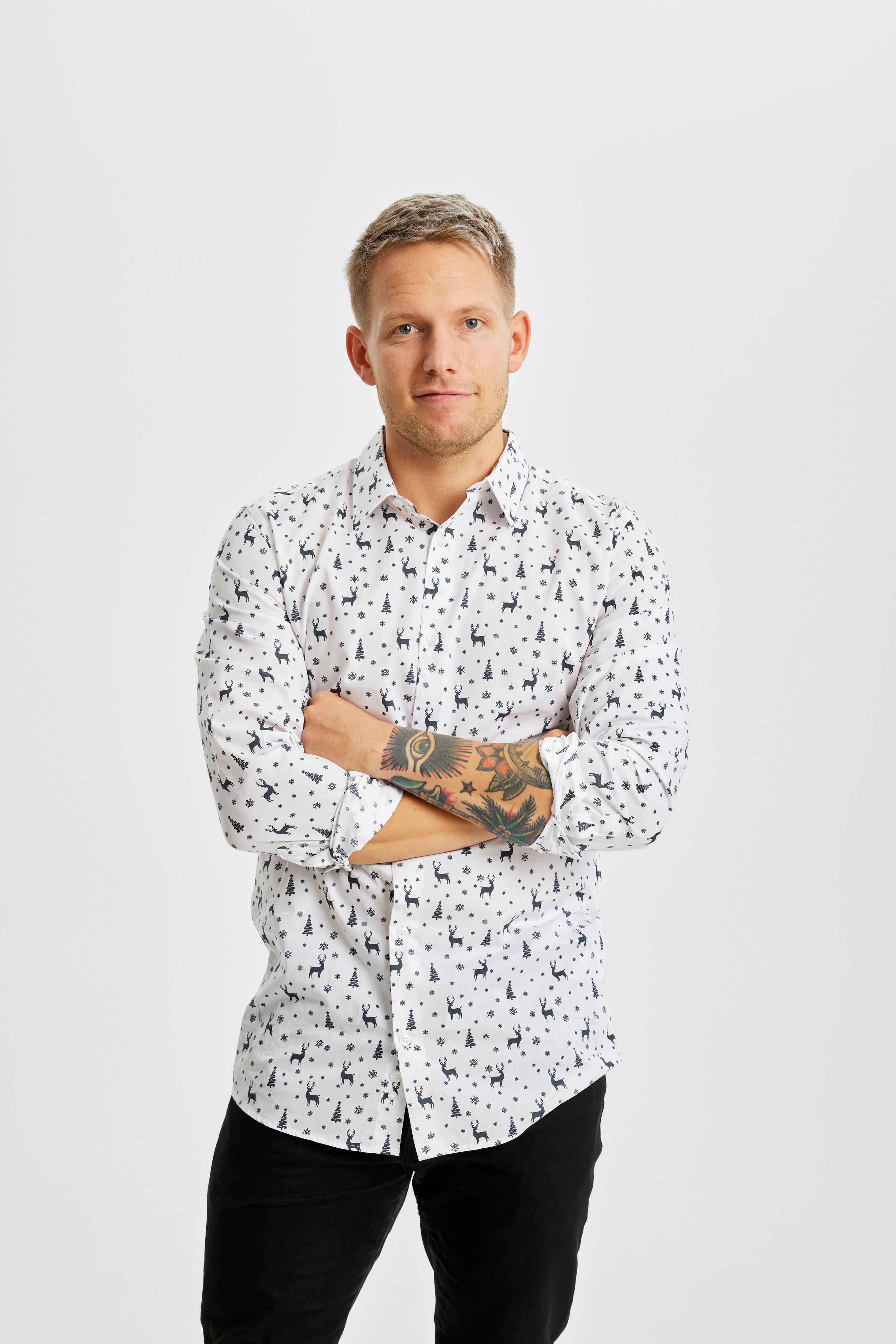 Un homme aux bras croisés portant une chemise de Noël blanche imprimée.