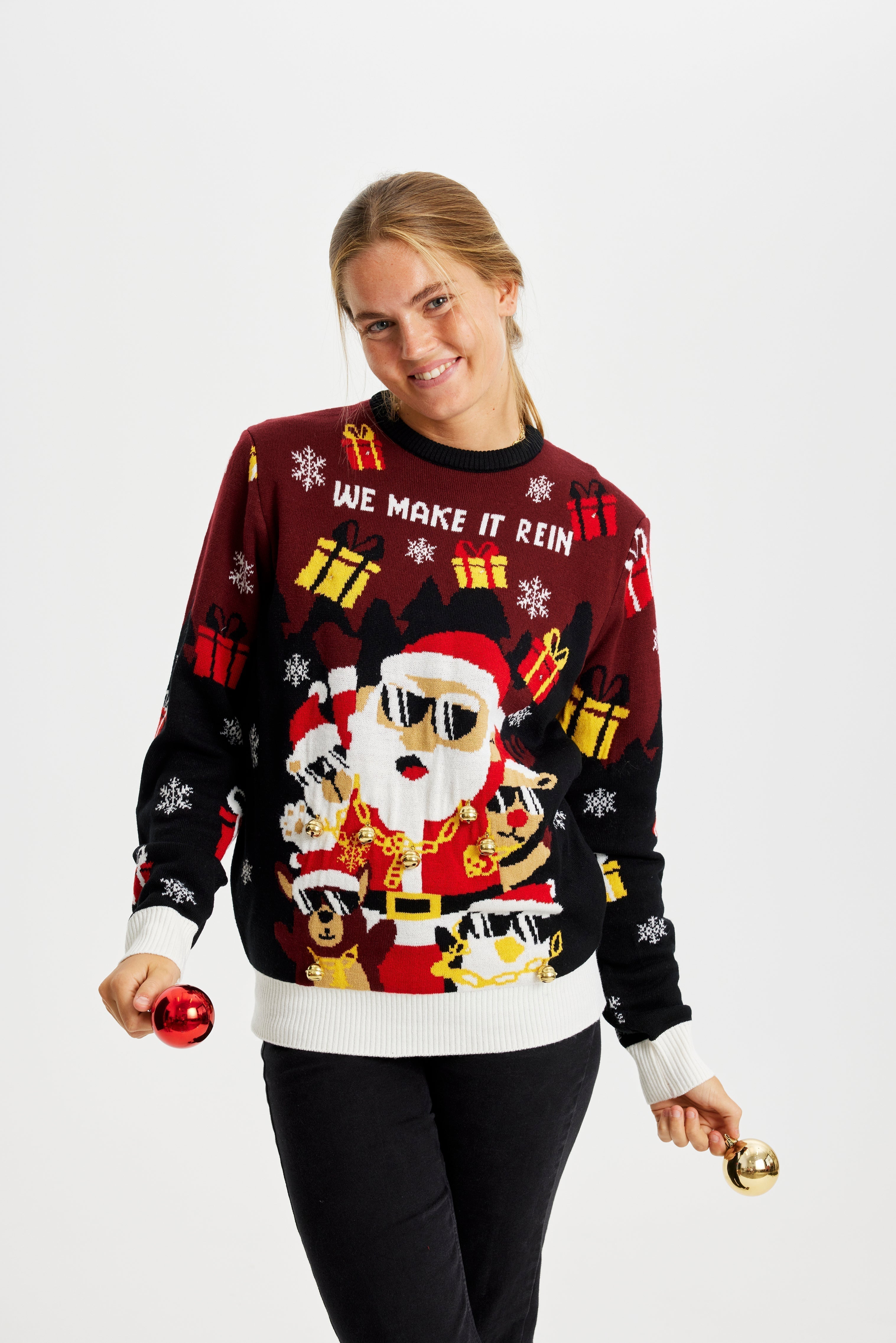 Une femme posant avec un pull de Noël rouge et noir avec le Père Noël et des lumières.