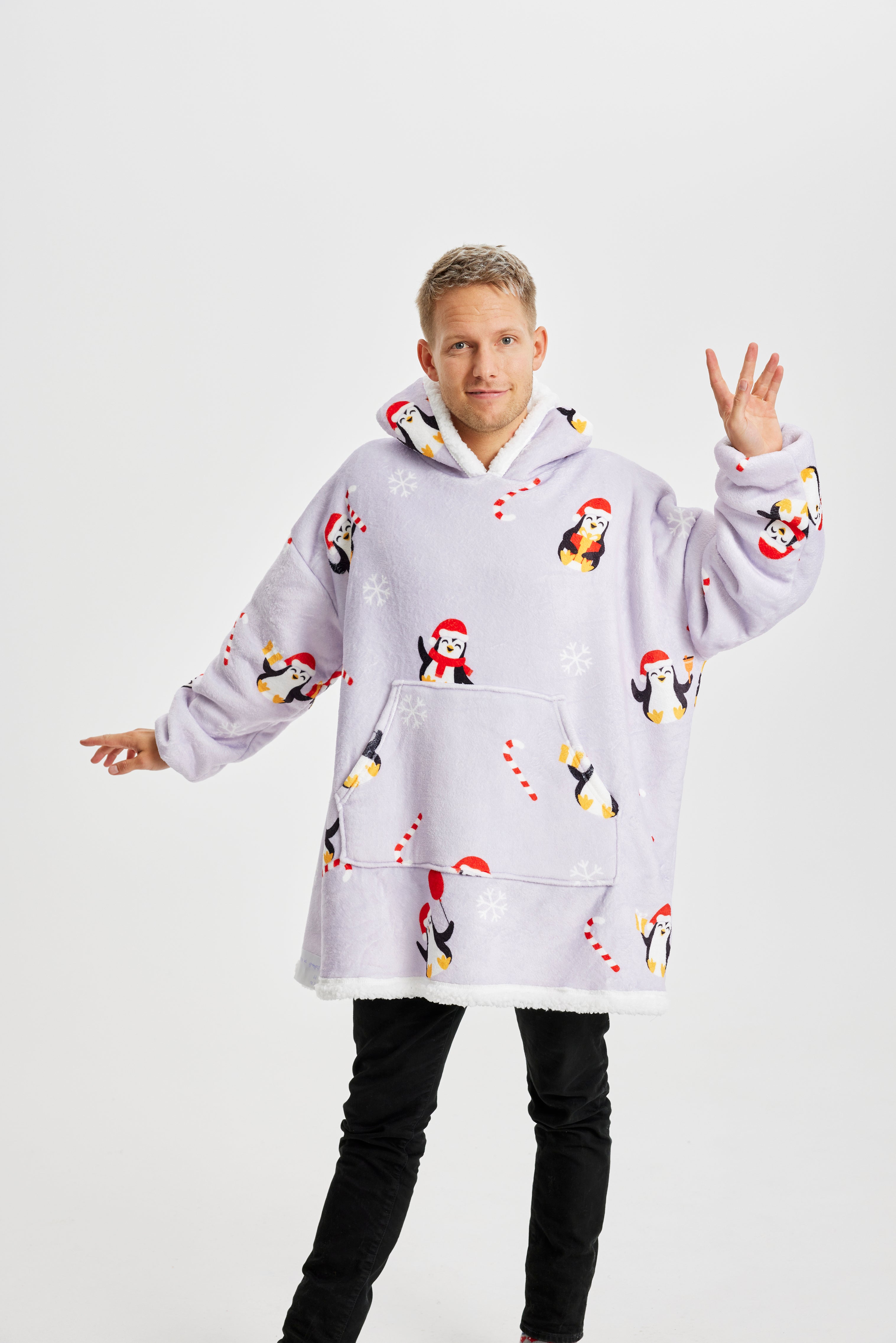 Un homme qui pose, portant un sweat à capuche de Noël violet clair avec des pingouins dessus.