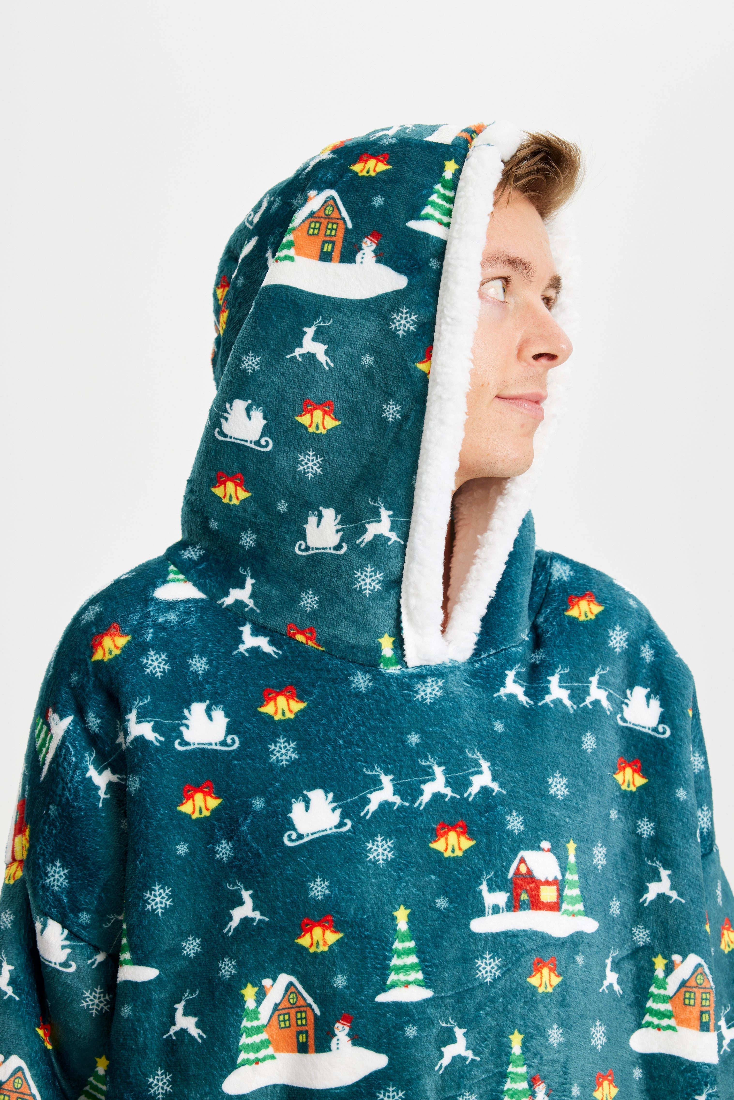 Un homme souriant regarde sur le côté, vêtu d'un sweat à capuche vert à motifs de Noël.