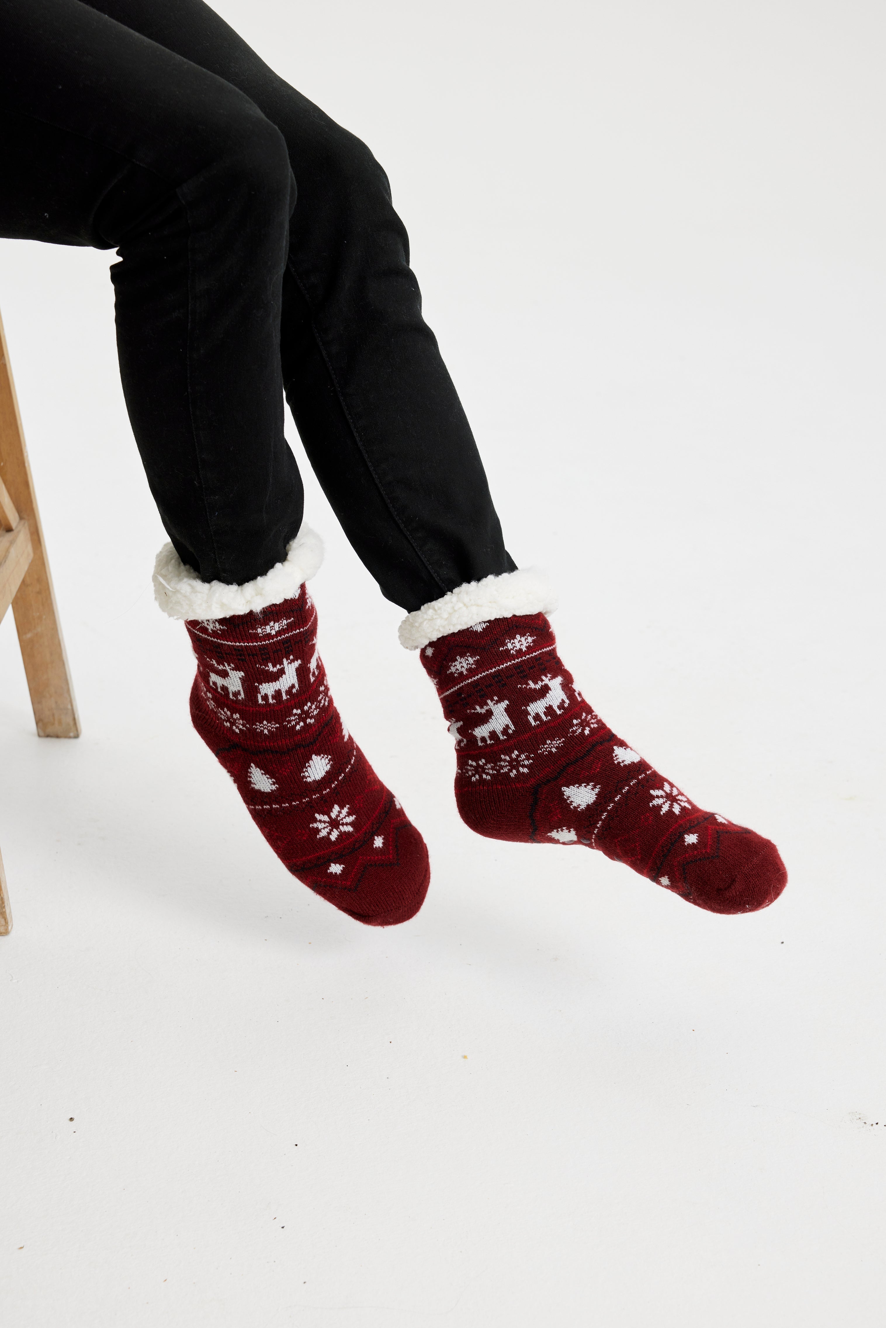 Une paire de pieds portant des chaussettes de Noël rouge foncé ornées de rennes et de cœurs.