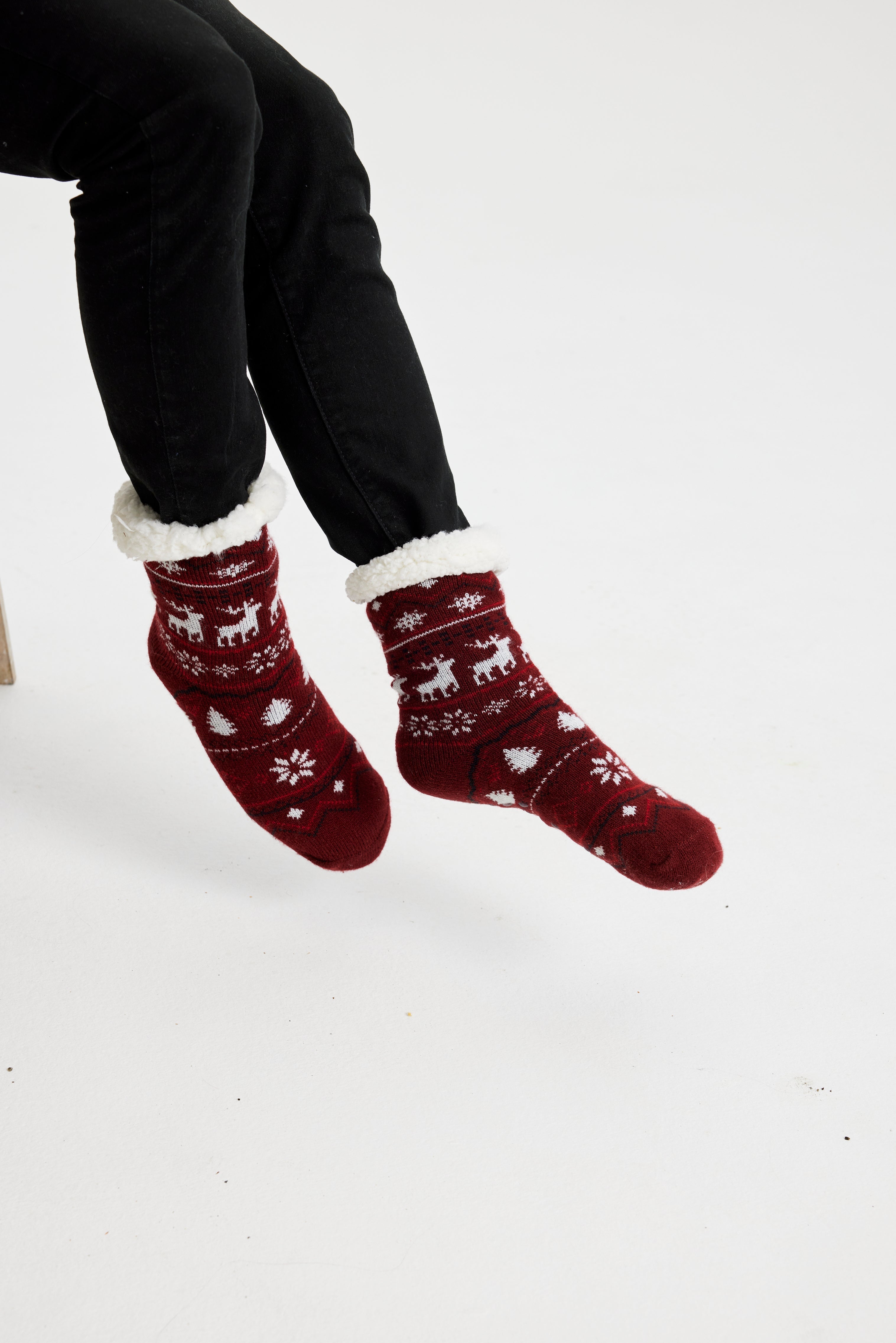 Une paire de pieds portant des chaussettes de Noël rouge foncé ornées de rennes et de cœurs.