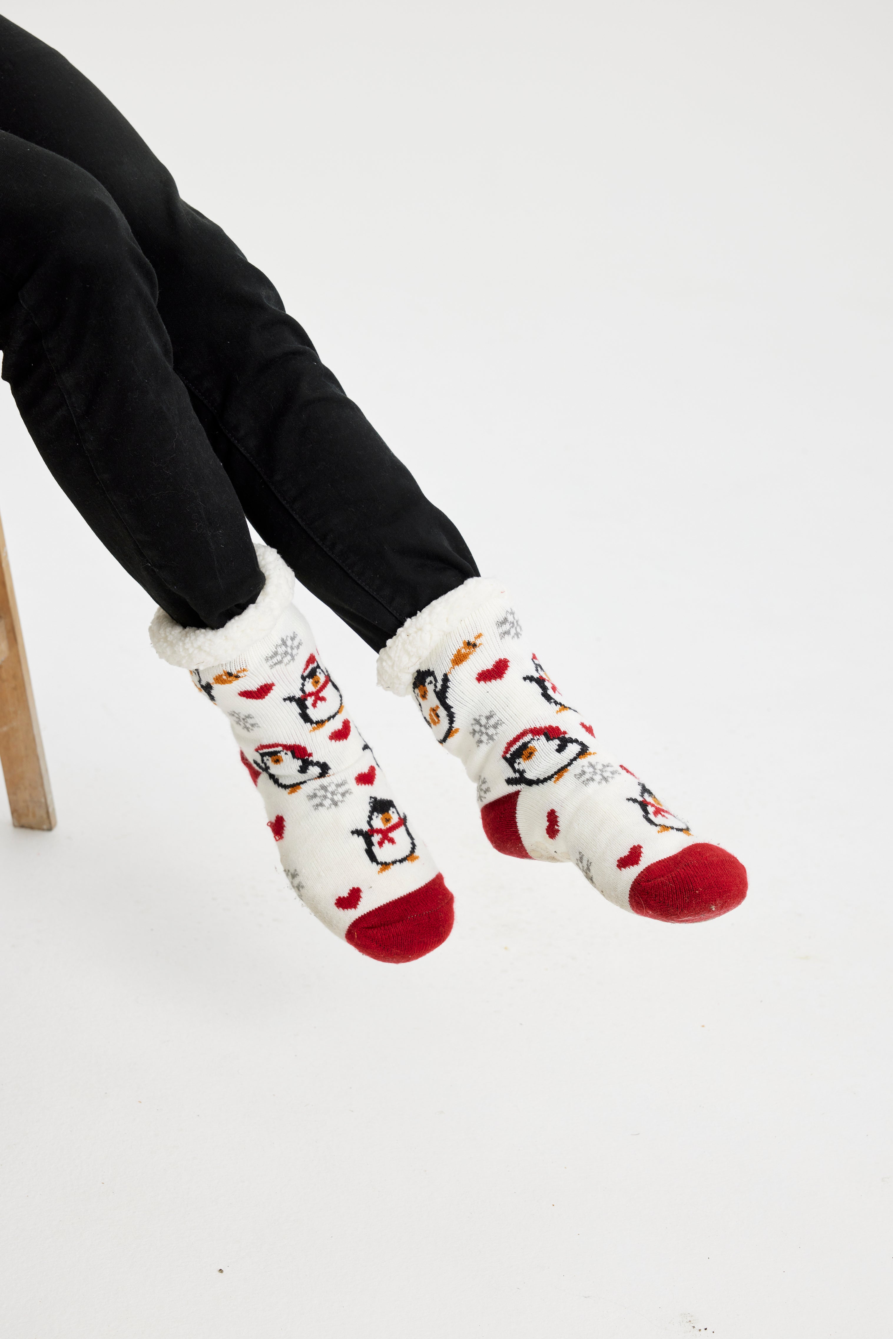 Une paire de pieds portant des chaussettes de Noël rouges et blanches ornées de pingouins.