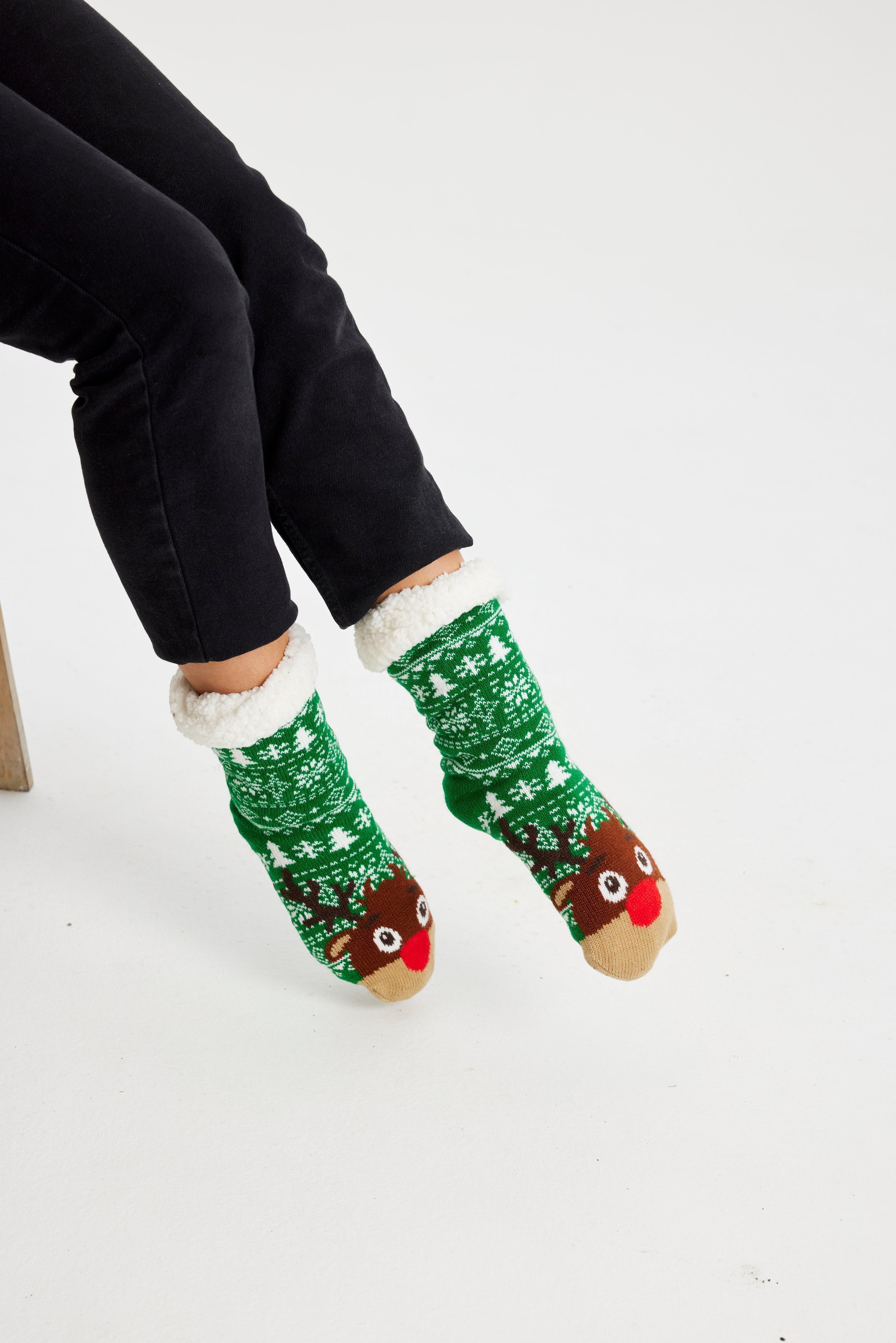 Une paire de pieds portant des chaussettes de Noël vertes ornées de Rudolph.
