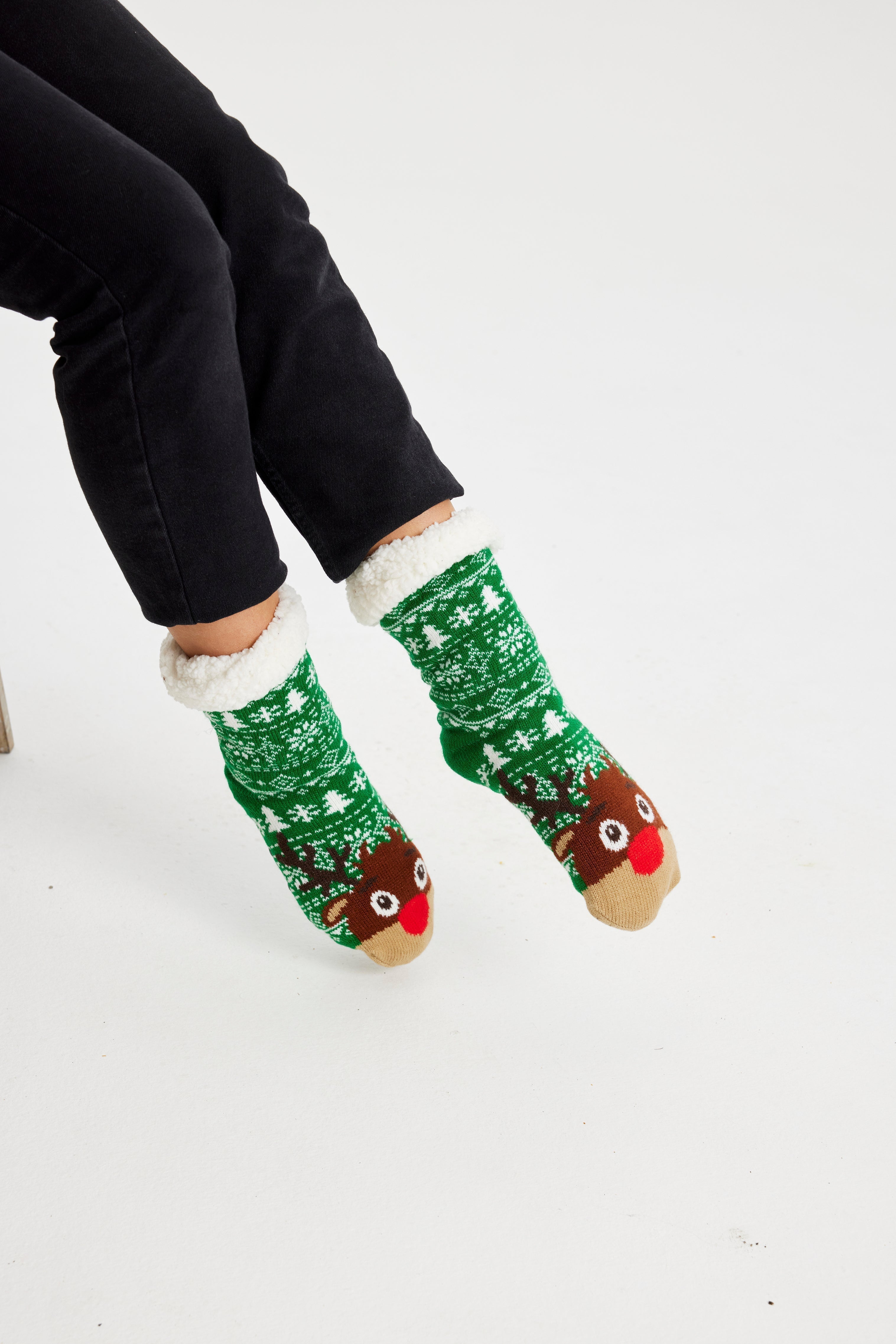 Une paire de pieds portant des chaussettes de Noël vertes ornées de Rudolph.