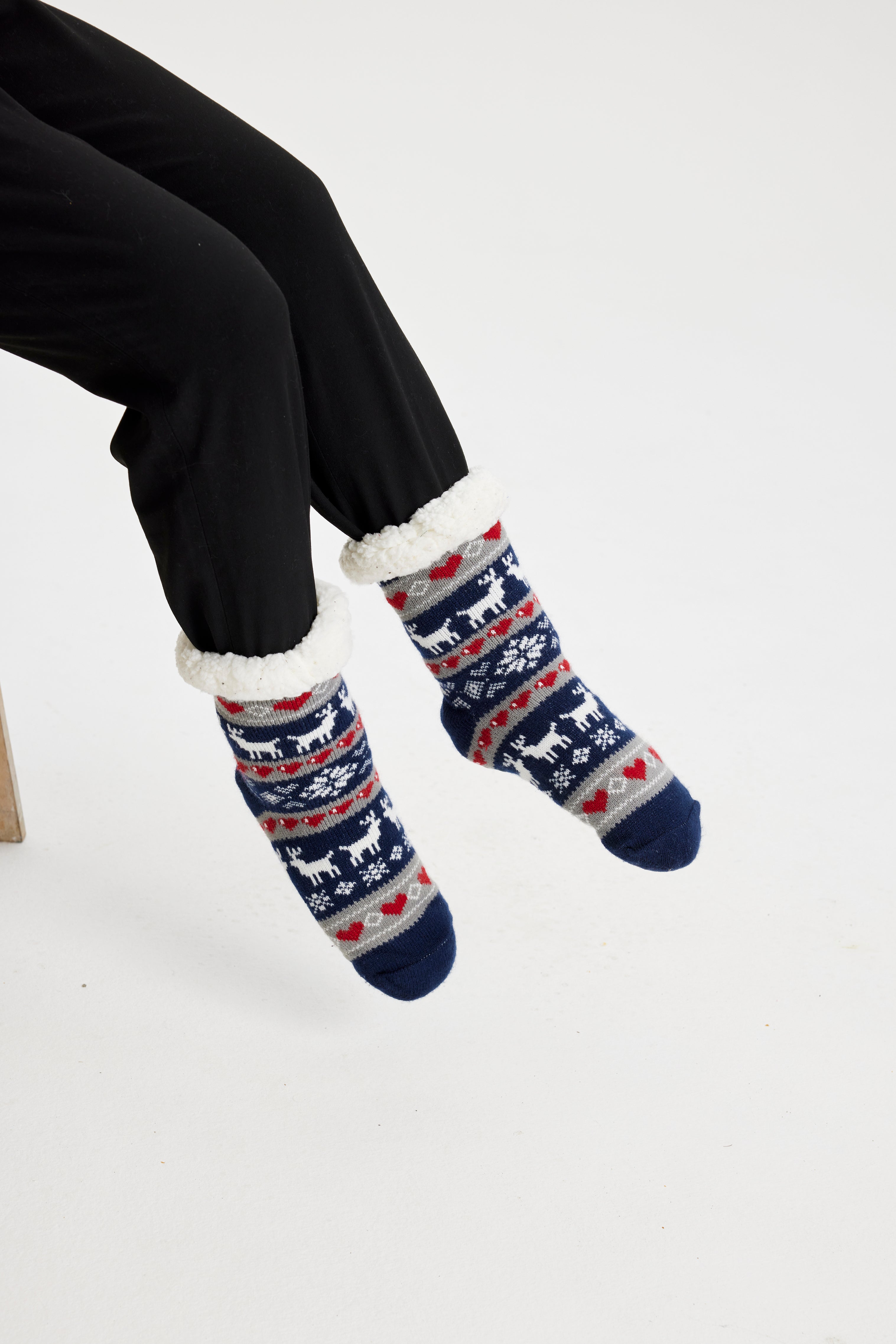 Une paire de pieds portant des chaussettes de Noël bleues ornées de rennes et de cœurs.