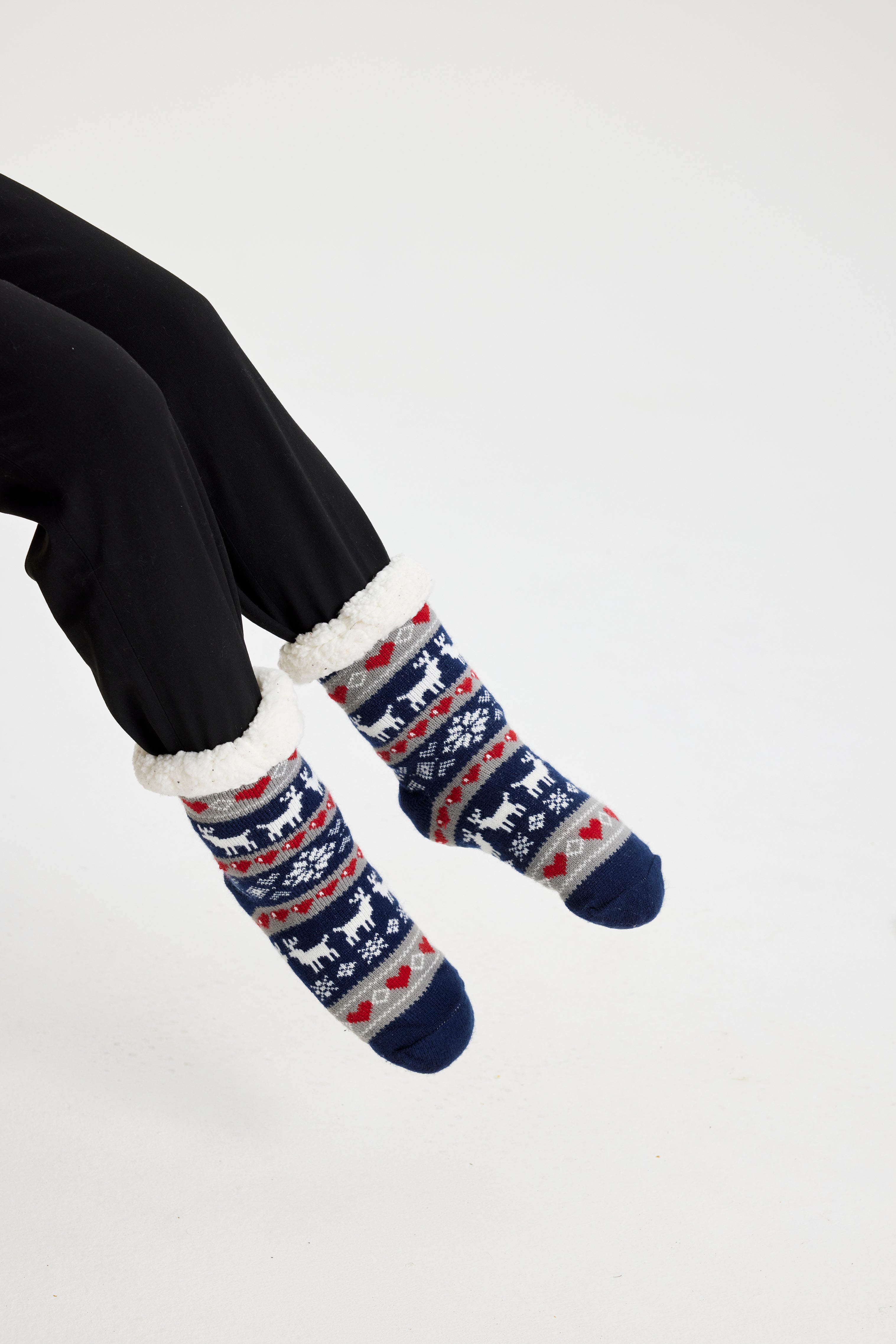 Une paire de pieds portant des chaussettes de Noël bleues ornées de rennes et de cœurs.