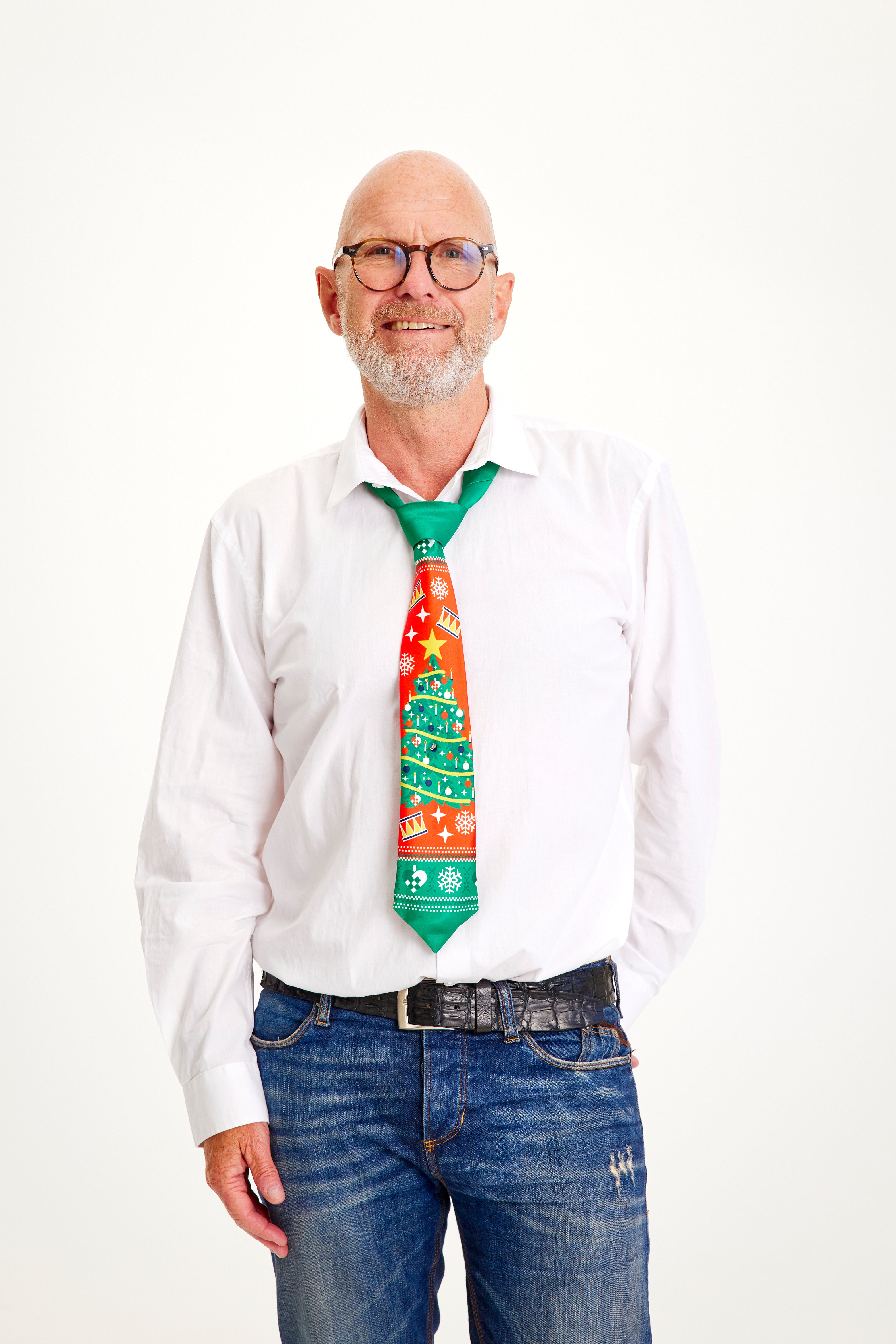 Un homme souriant en chemise blanche portant une cravate de Noël à motifs rouges et verts.