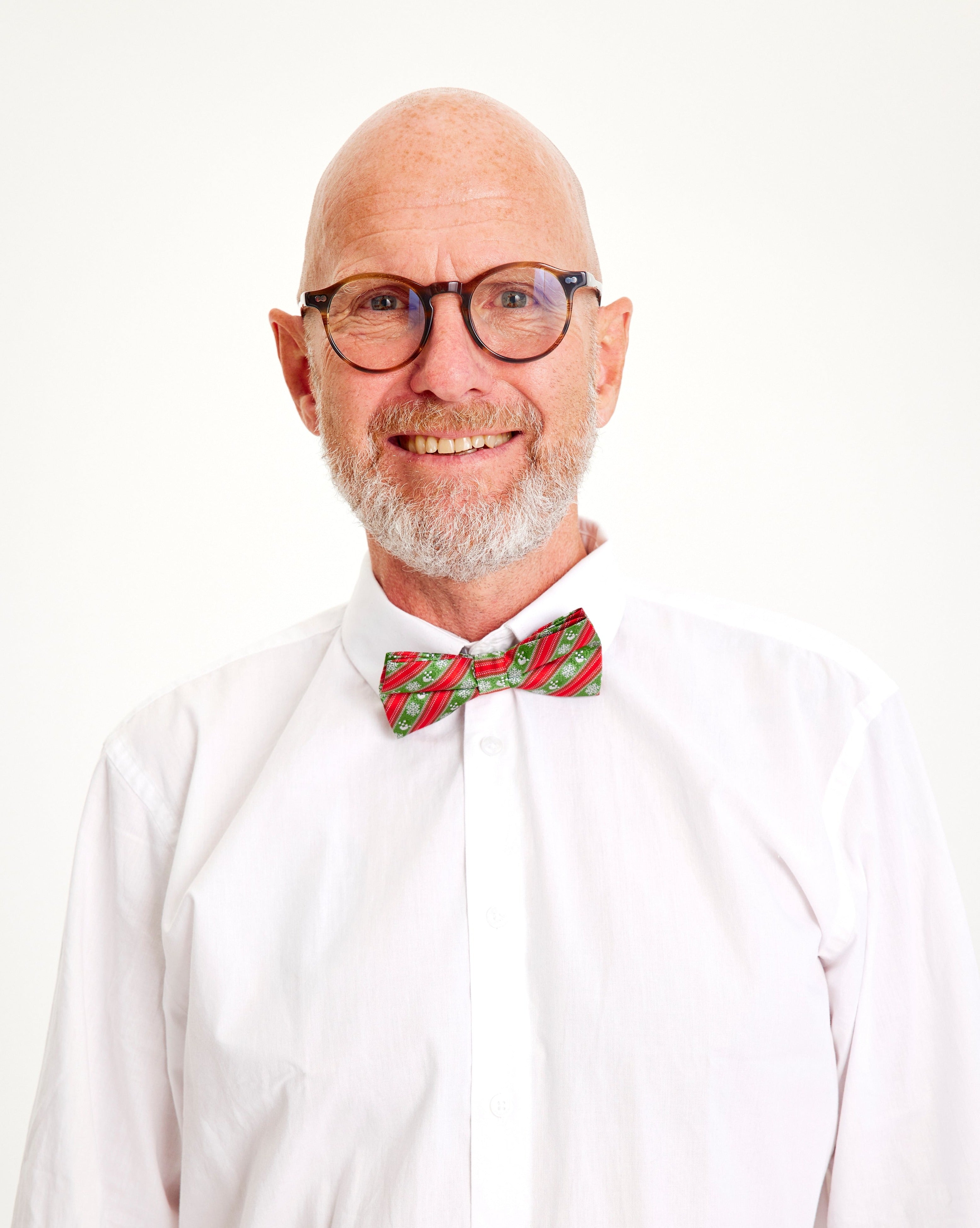 Un homme souriant portant un nœud papillon rouge et vert.