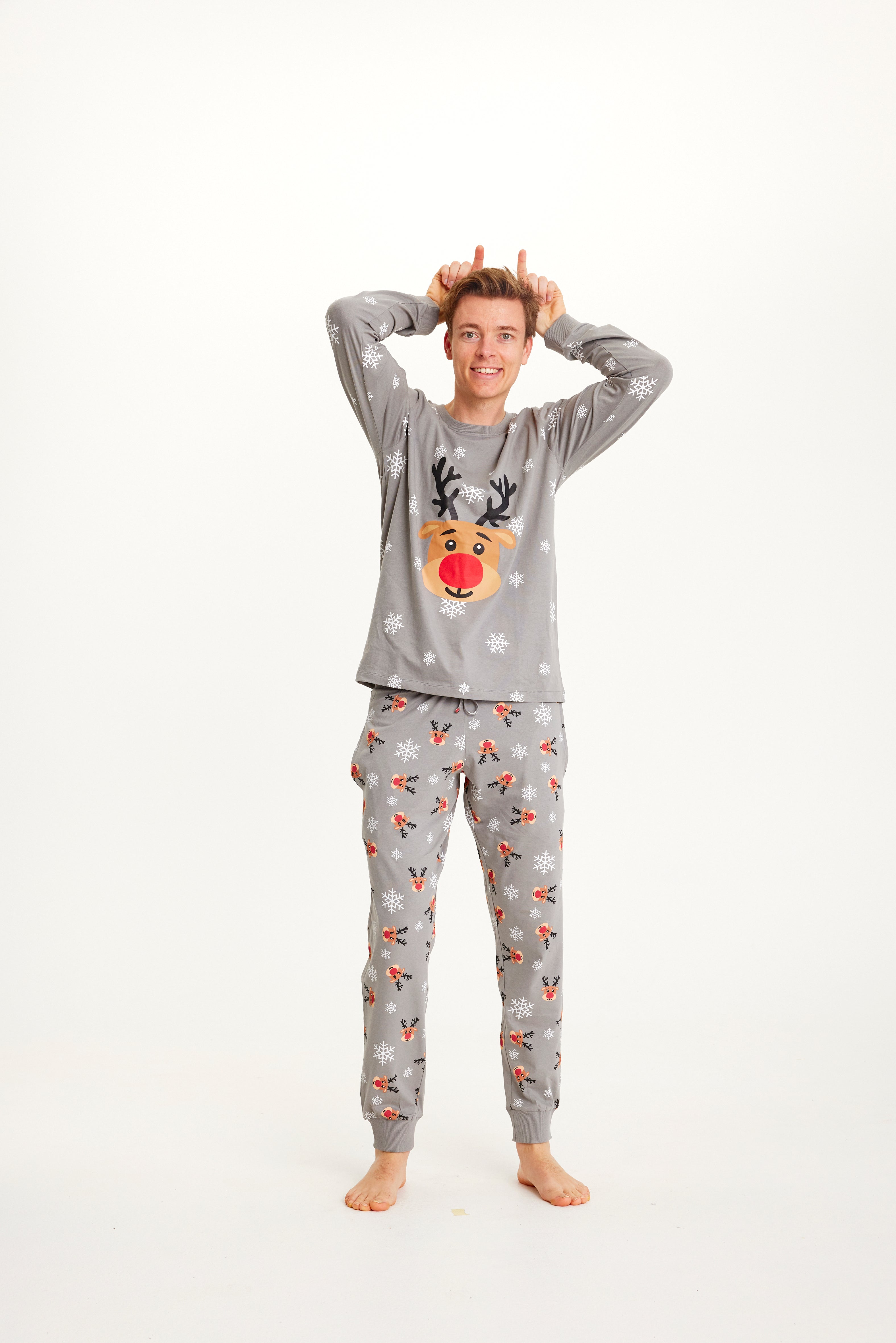 Un homme posant portant un pyjama de Noël gris avec Rudolph.