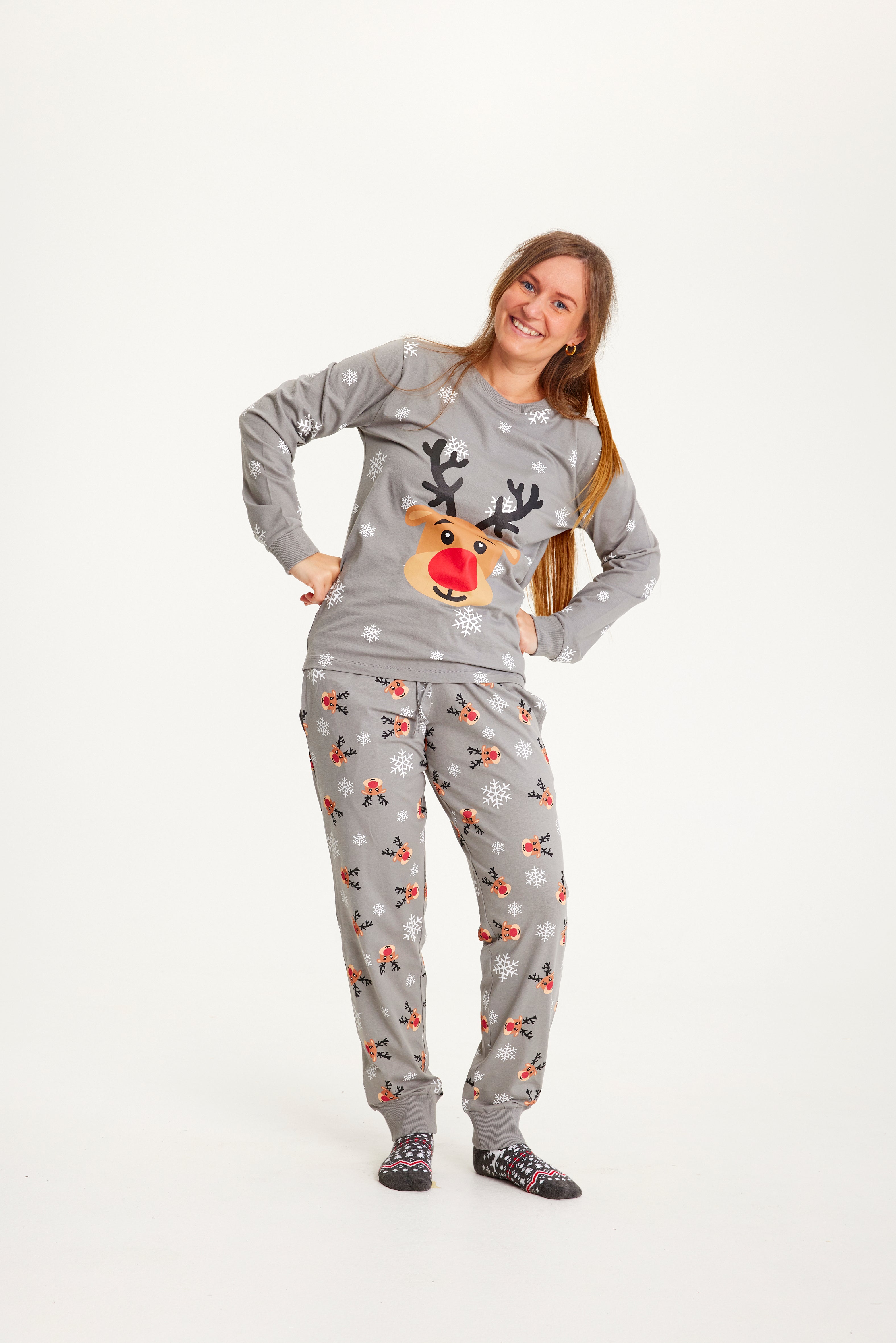 Une femme, les mains le long du corps, portant un pyjama de Noël gris avec Rudolph.