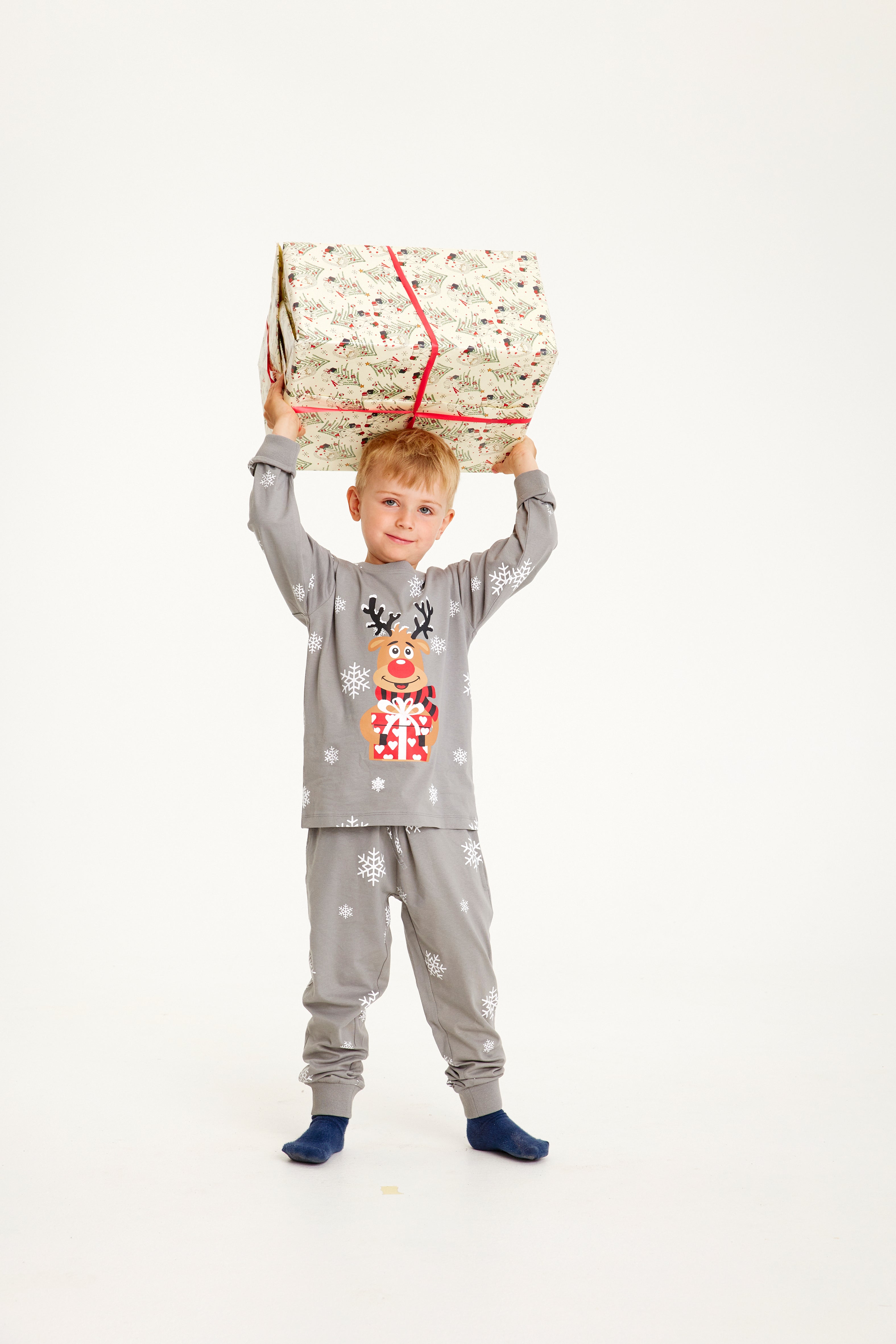 Un enfant avec un cadeau portant un pyjama de Noël gris avec Rudolph.