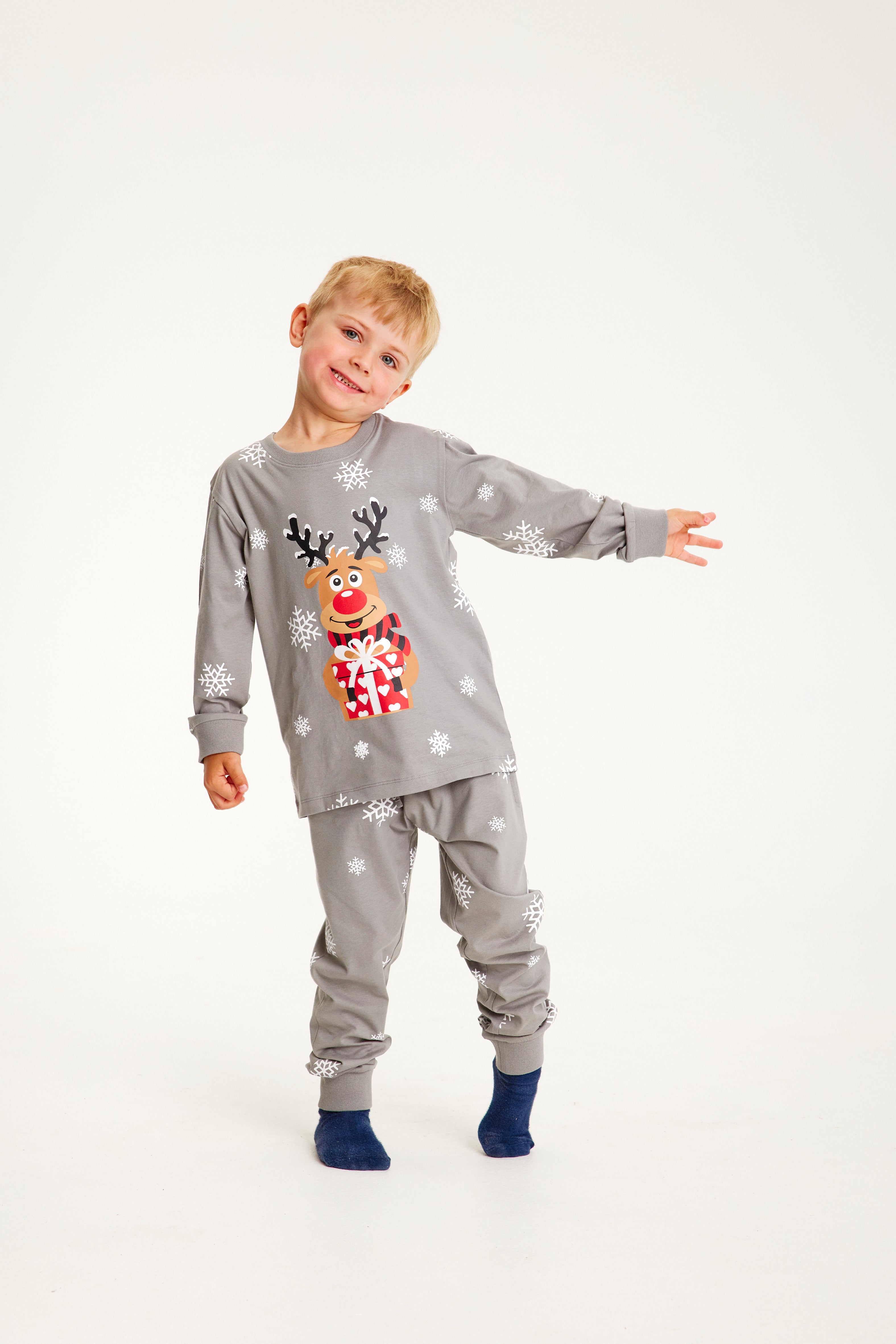 Un enfant posant avec un pyjama de Noël gris orné de Rudolph.