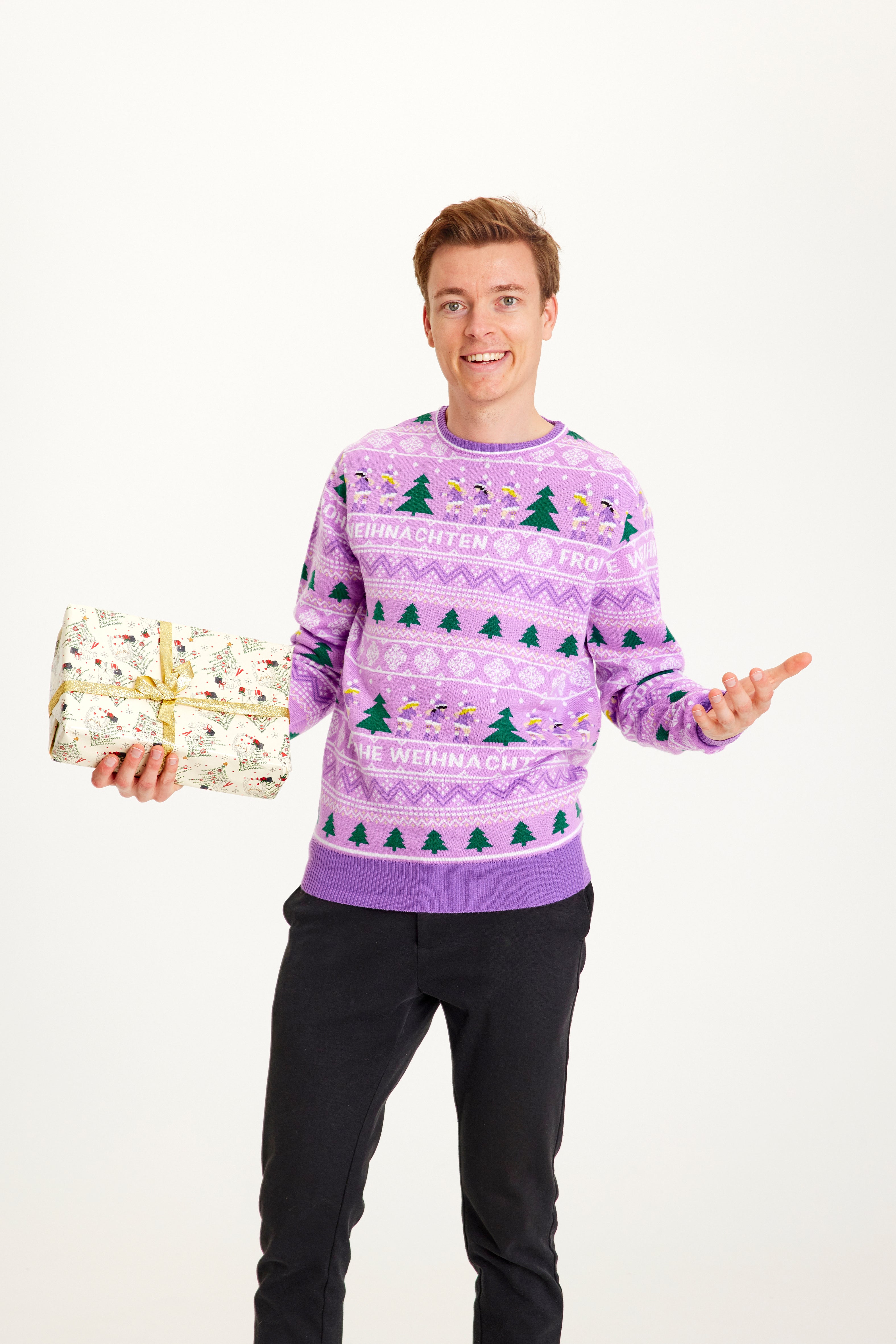 En smilende ung mand med en gave i hånd iført en lilla julesweater.