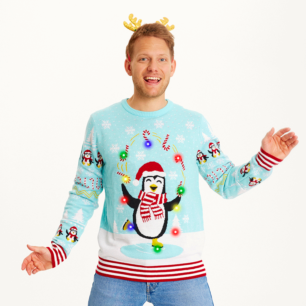 Un homme portant un pull de Noël bleu clair avec des pingouins et des lumières.