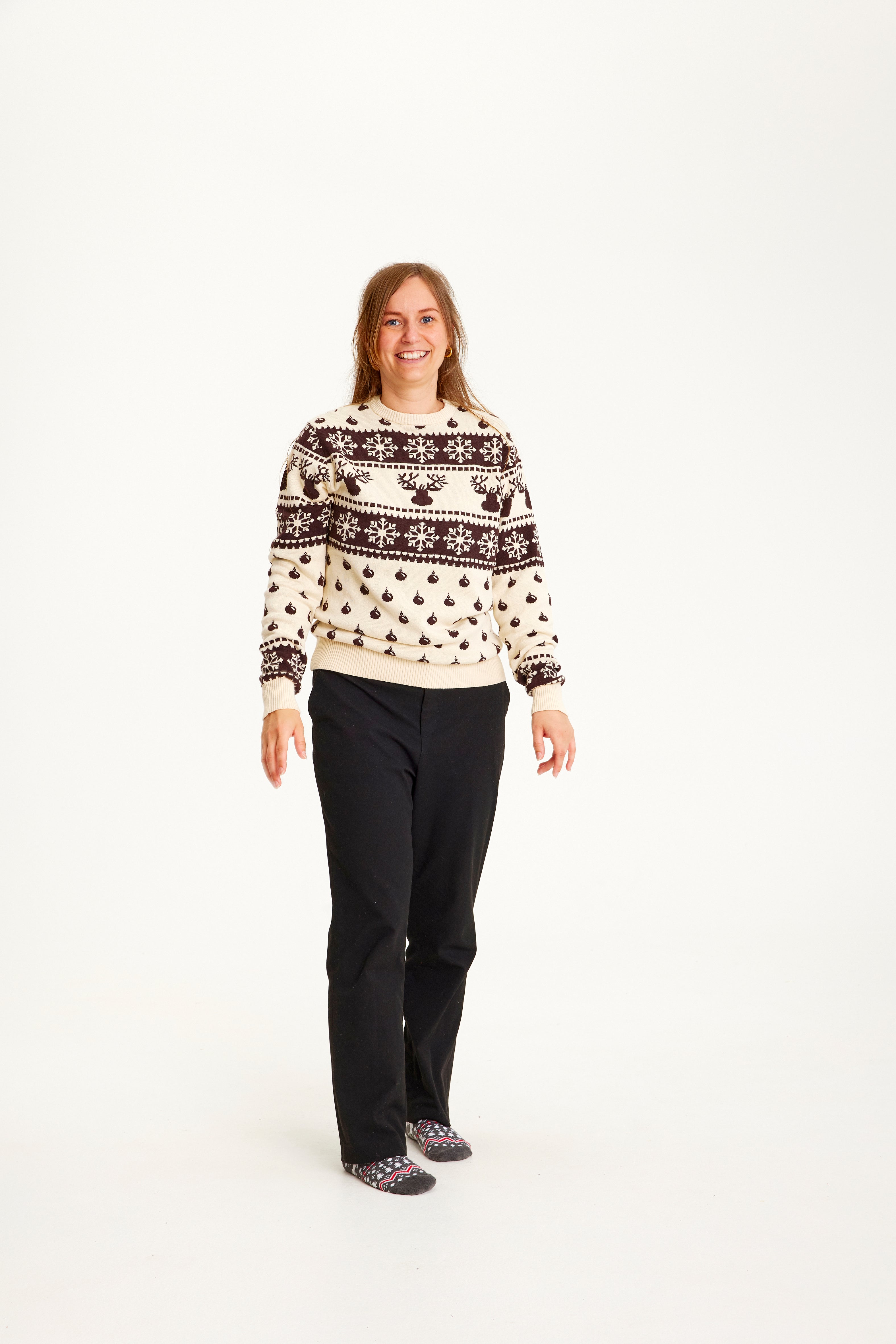 Une femme posant avec un pull de Noël beige et marron avec des flocons de neige et des motifs.