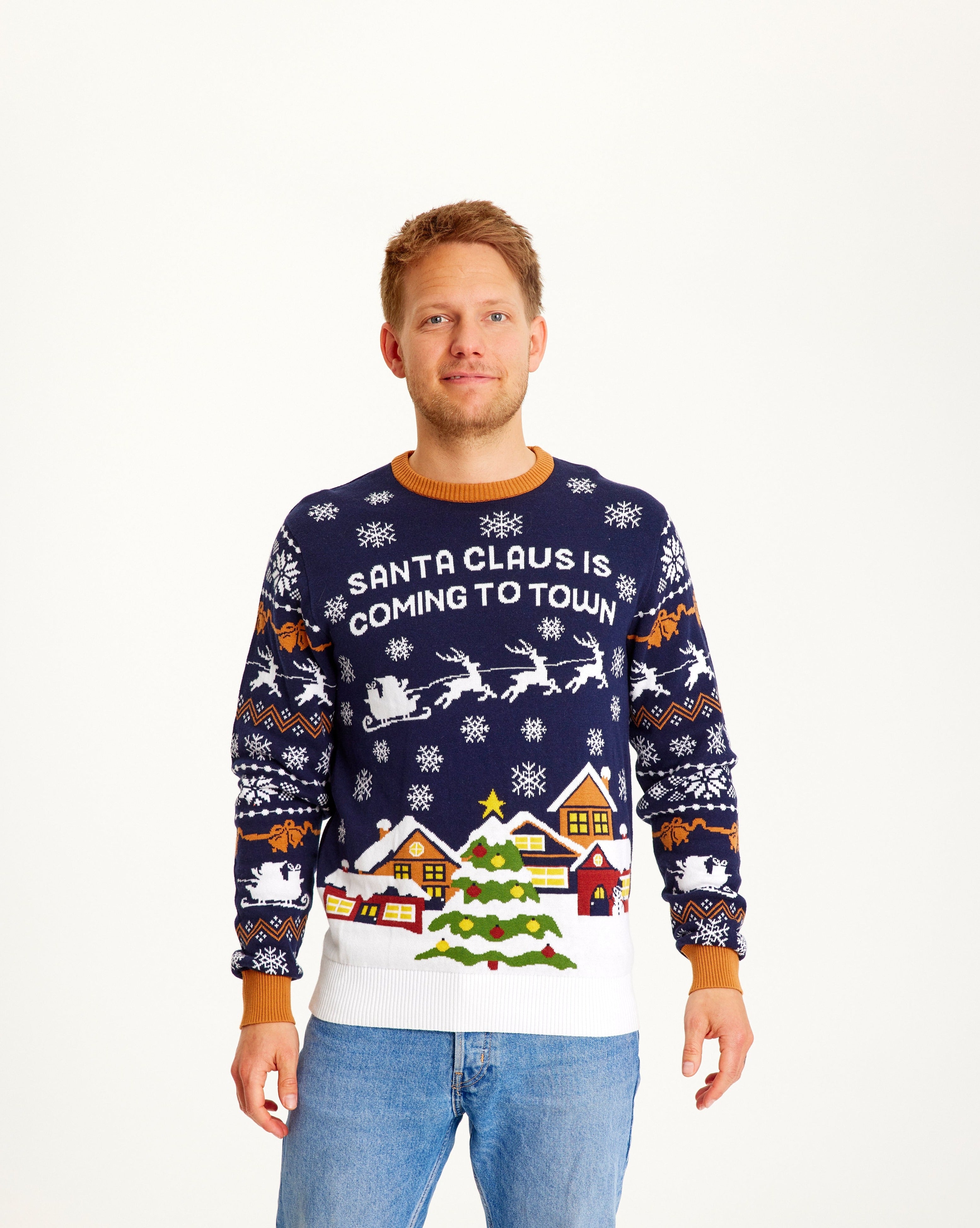 Homme posant avec un pull de Noël bleu foncé et blanc orné d'un arbre de Noël.